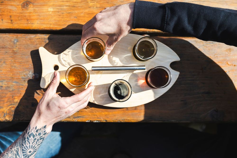 People enjoying a beer flight sampling with various dark and light craft brews on a wooden table at a brewery.