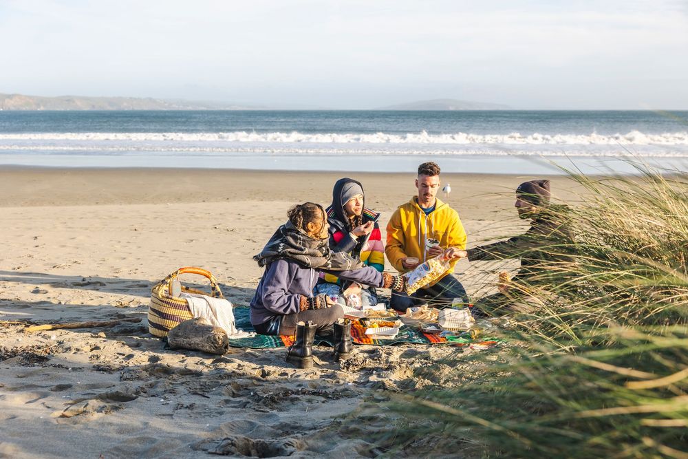 People relaxing and enjoying a sunny day at a scenic beach with sand dunes and ocean waves.