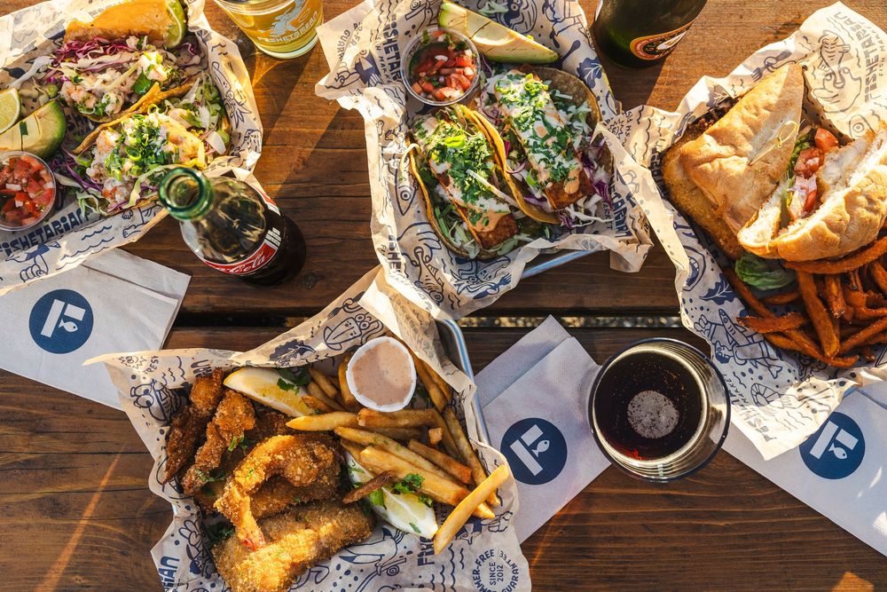 Overhead view of fish and chips with french fries and dipping sauces served on wooden table with paper wrapping.