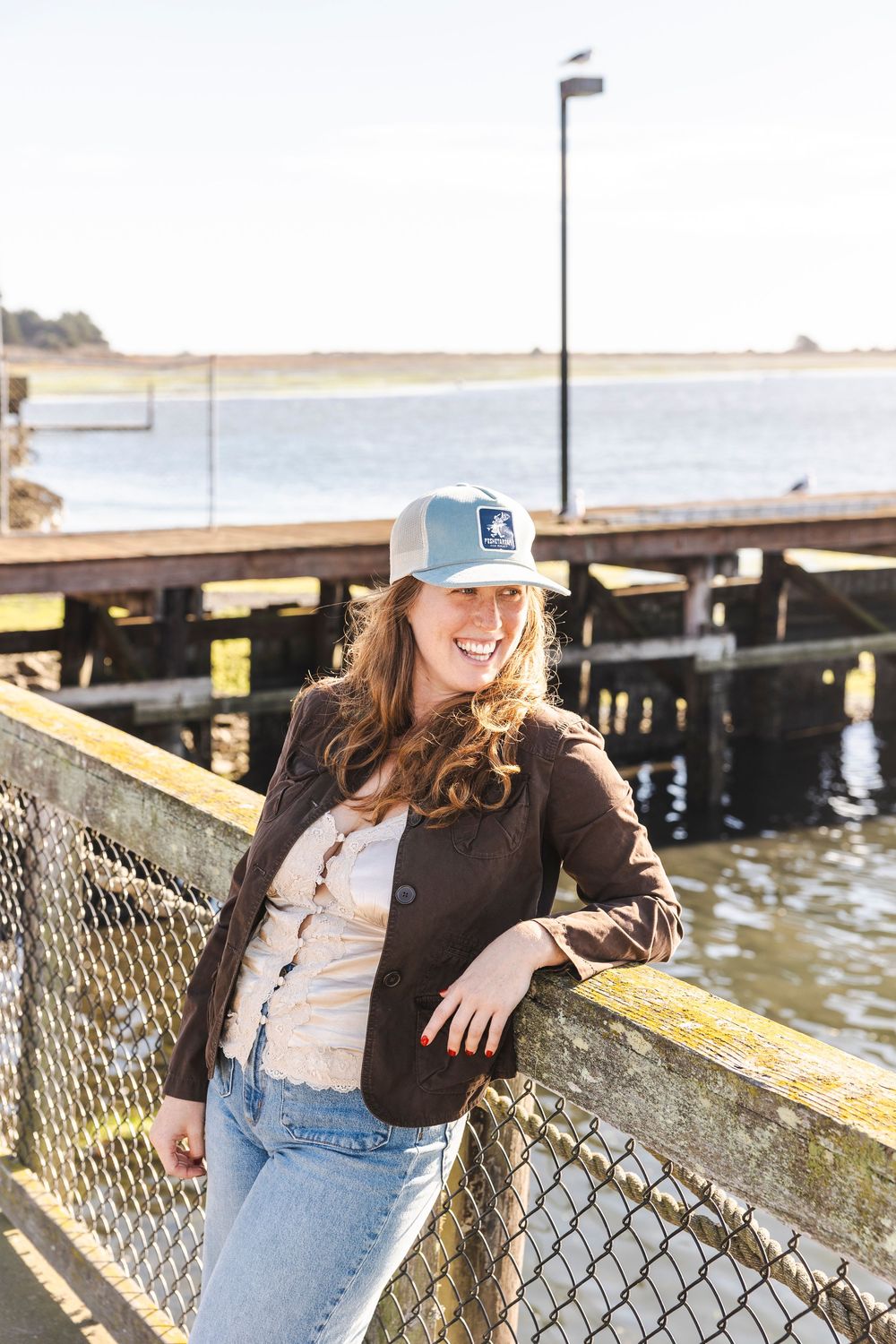 Casual lifestyle photo series showing someone in jeans and baseball cap leaning against coastal railing at sunset.