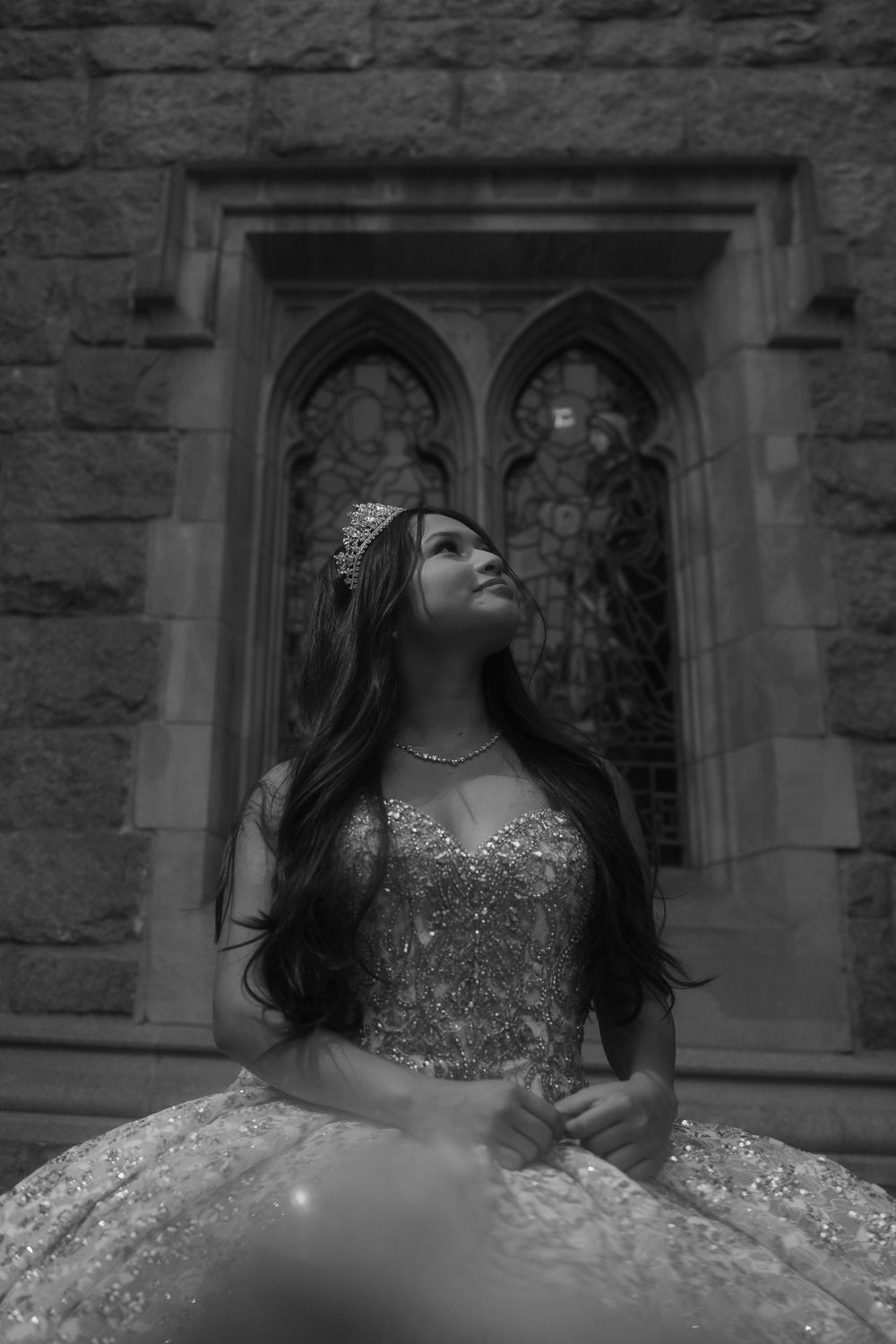 Elegant formal gown with sparkly details and tiara photographed in black and white against gothic stone church architecture.