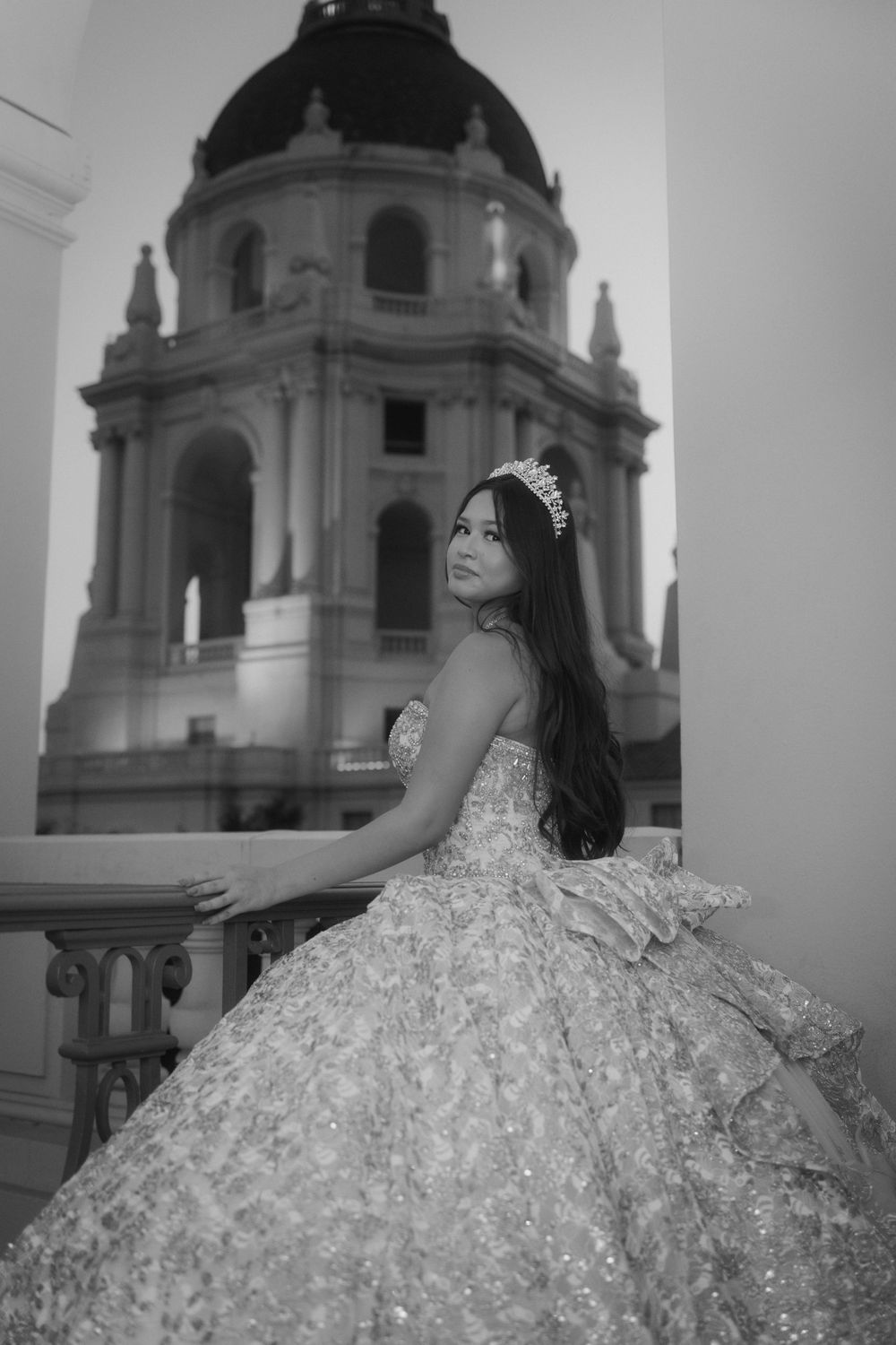 Black and white photo of a person in a sparkly quinceanera gown posing in front of a beautiful domed church building.