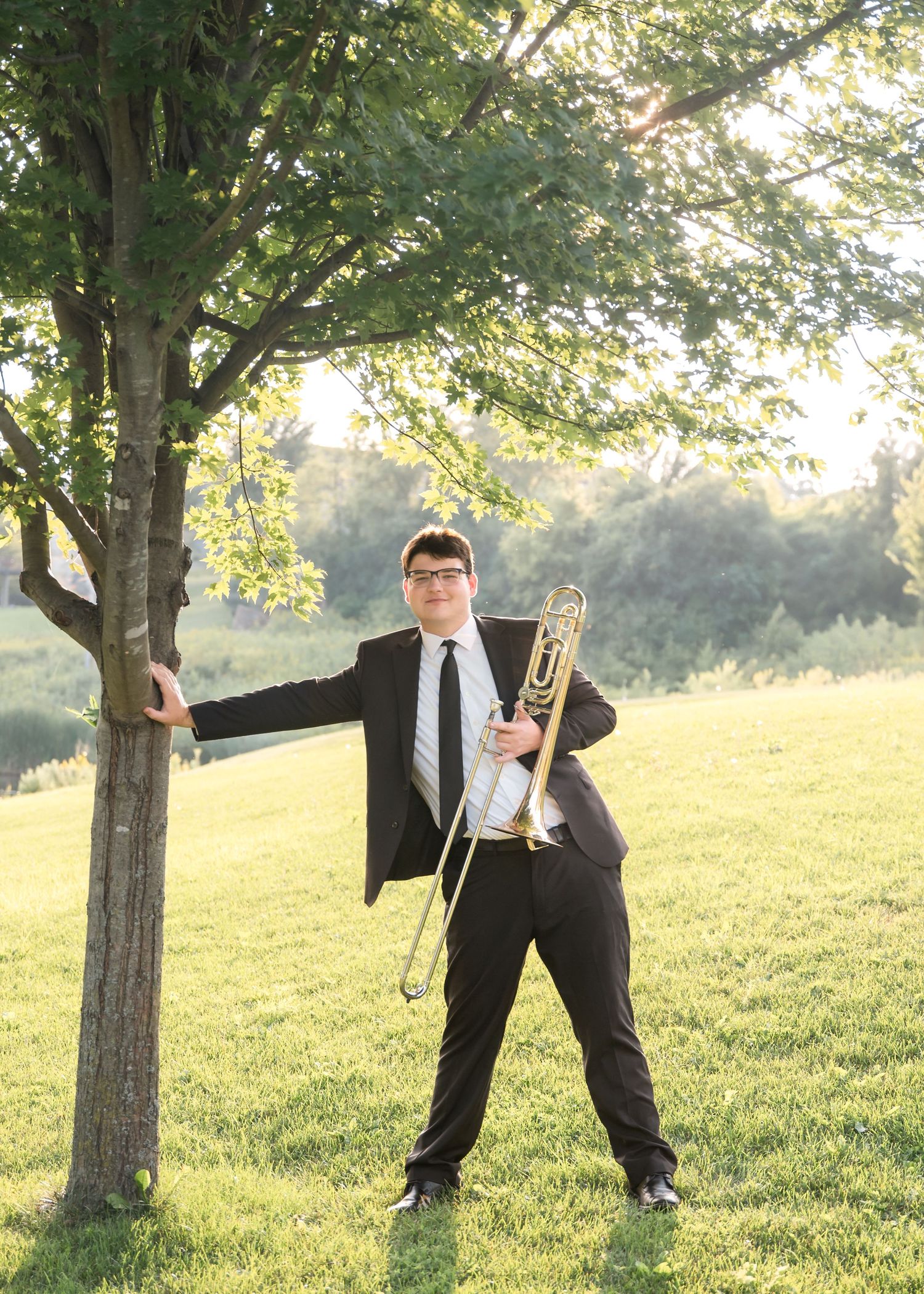 A businessman poses playfully behind a tree in a park at sunset, showing a sequence of dance-like movements.