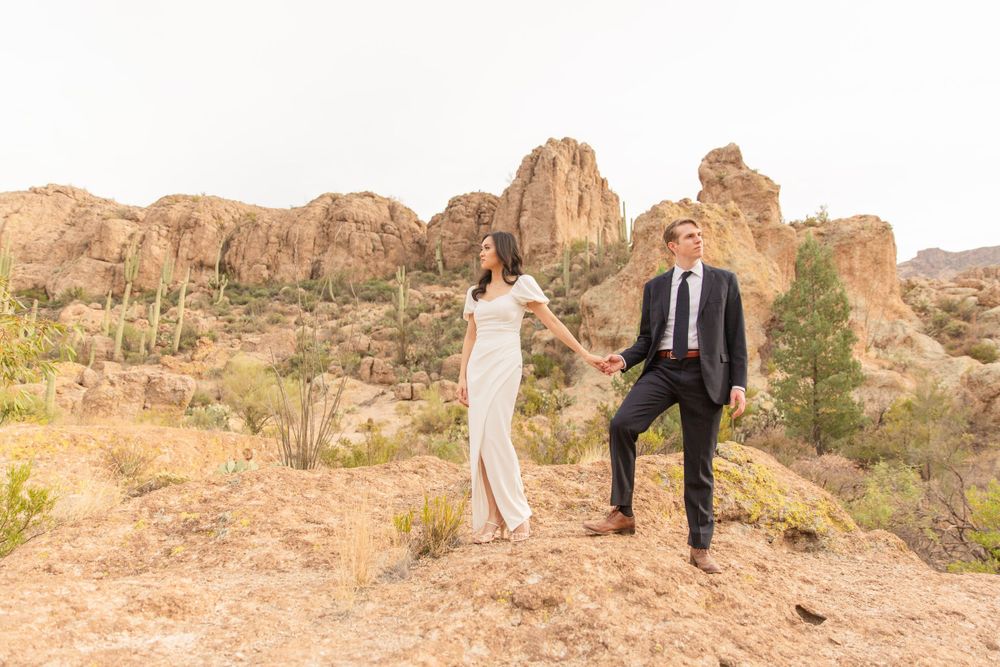 A couple in formal wear standing on rocky desert terrain with mountain views.