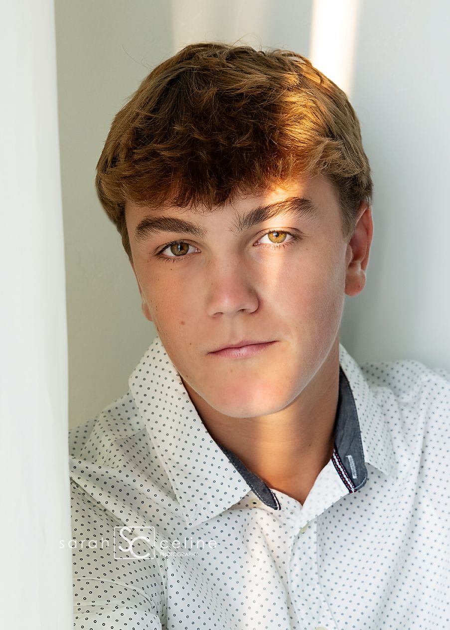 Person wearing a white polka dot collared shirt poses for a close-up portrait against a white background.
