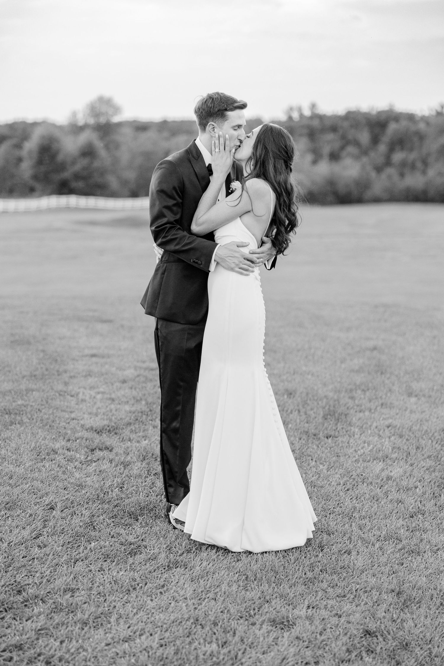 A couple in wedding attire embraces as they dance on an open field in black and white.