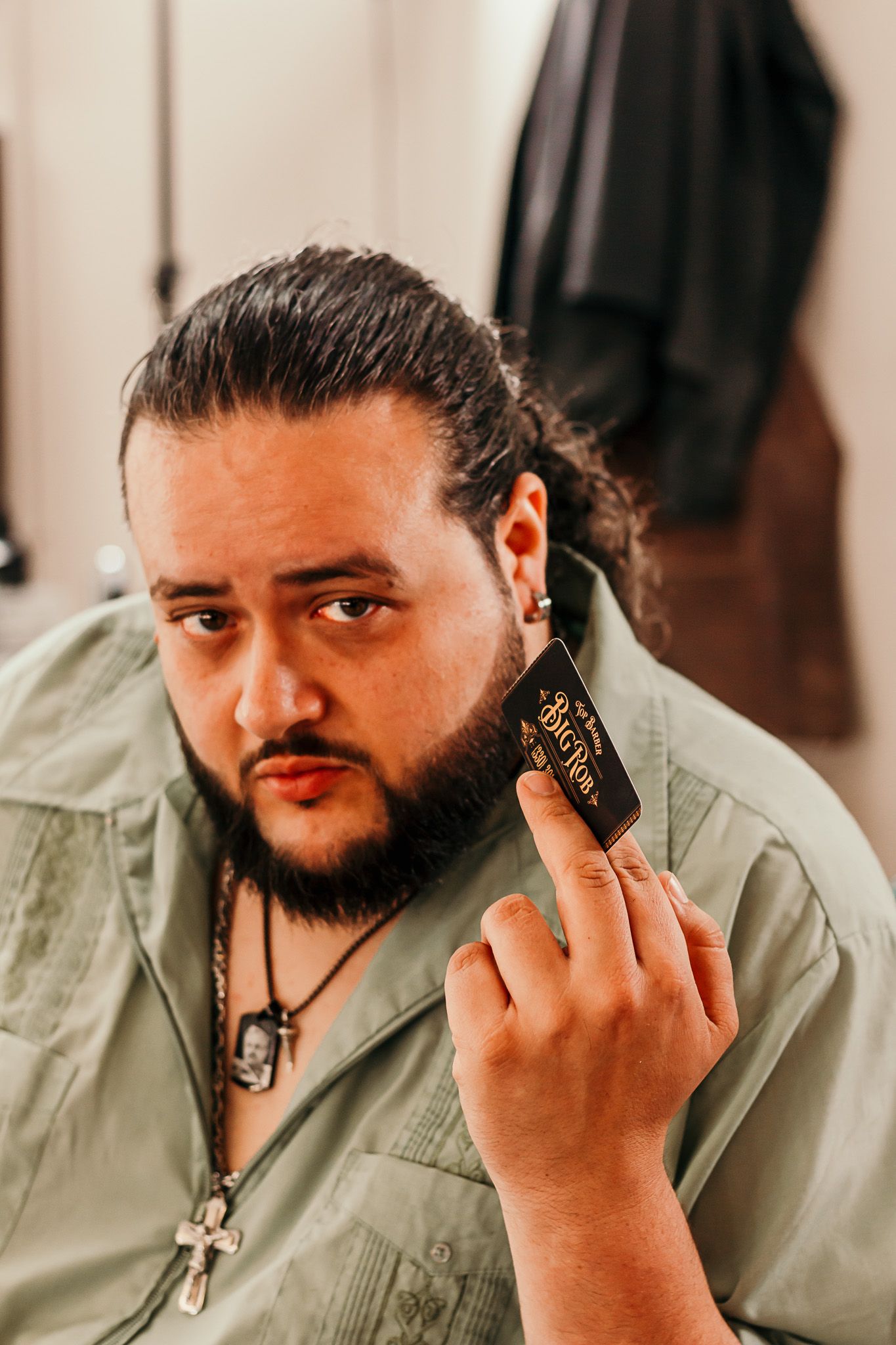 A man in a green shirt holds up a dark vape device while posing for a casual portrait photo.