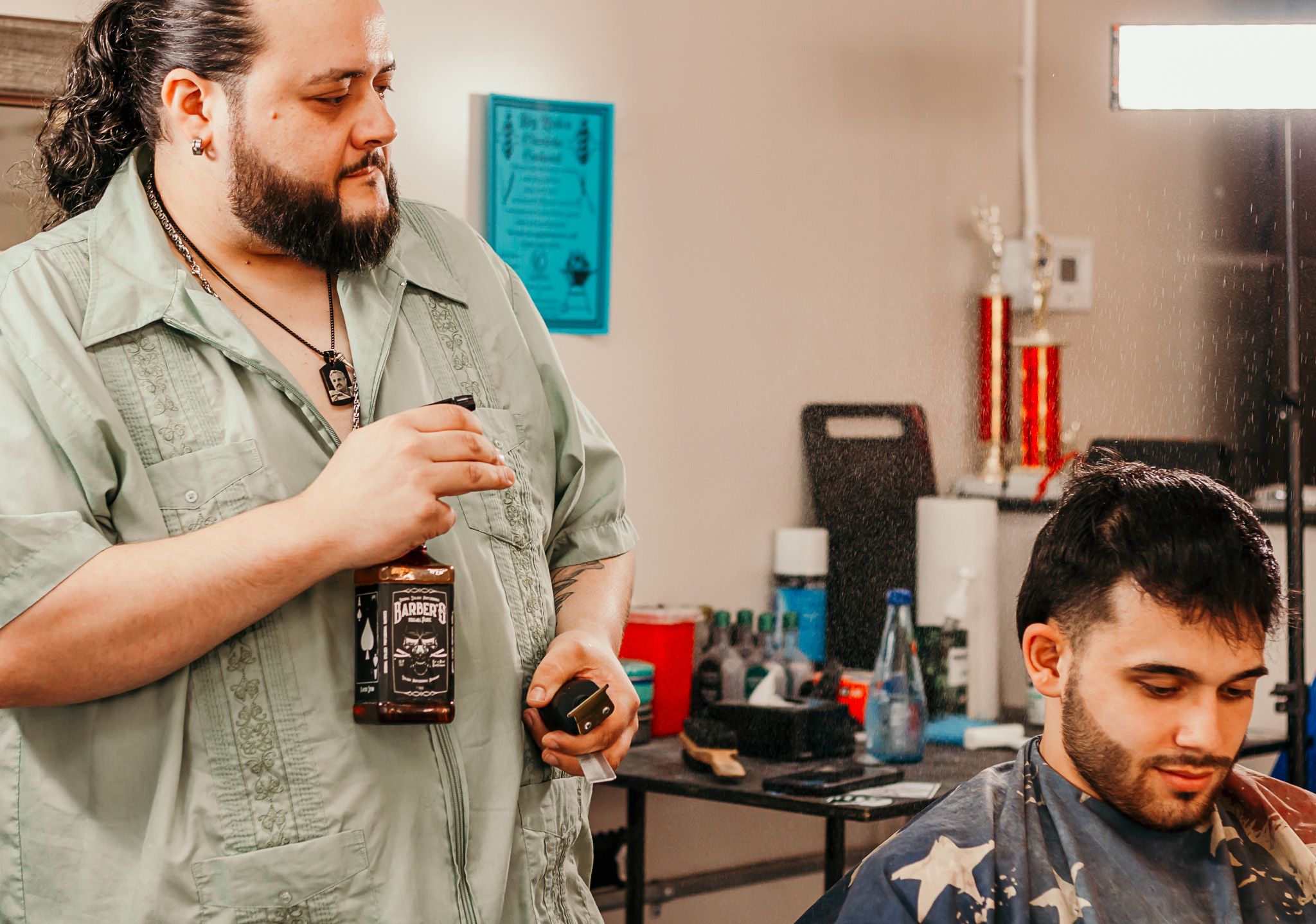 Barber holding barber tools stands in front of client chair in modern salon with turquoise wall accents in background.