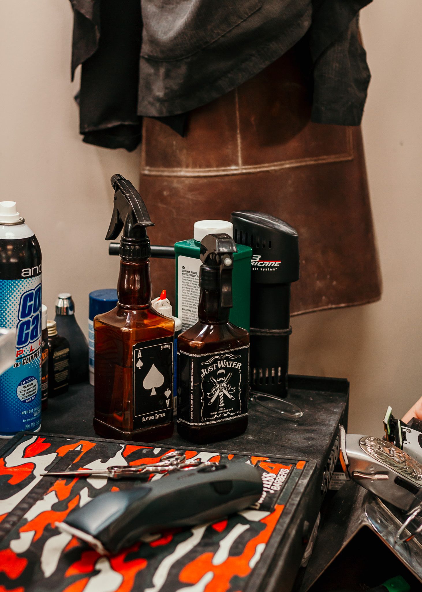 A cluttered barber station with Jack Daniel's bottles, hair products, and styling tools on a dark counter.