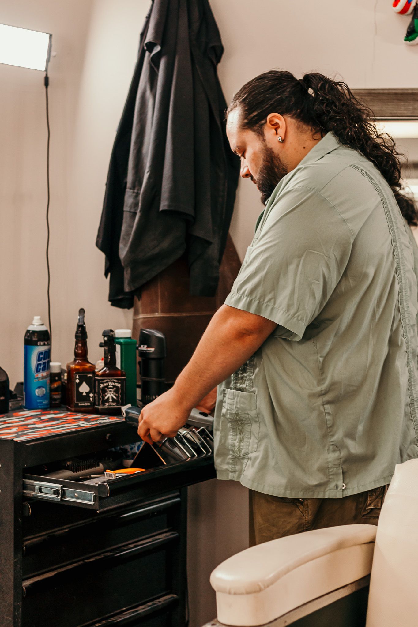 Barber organizing and arranging tools and equipment at vintage wooden workstation in traditional barbershop.
