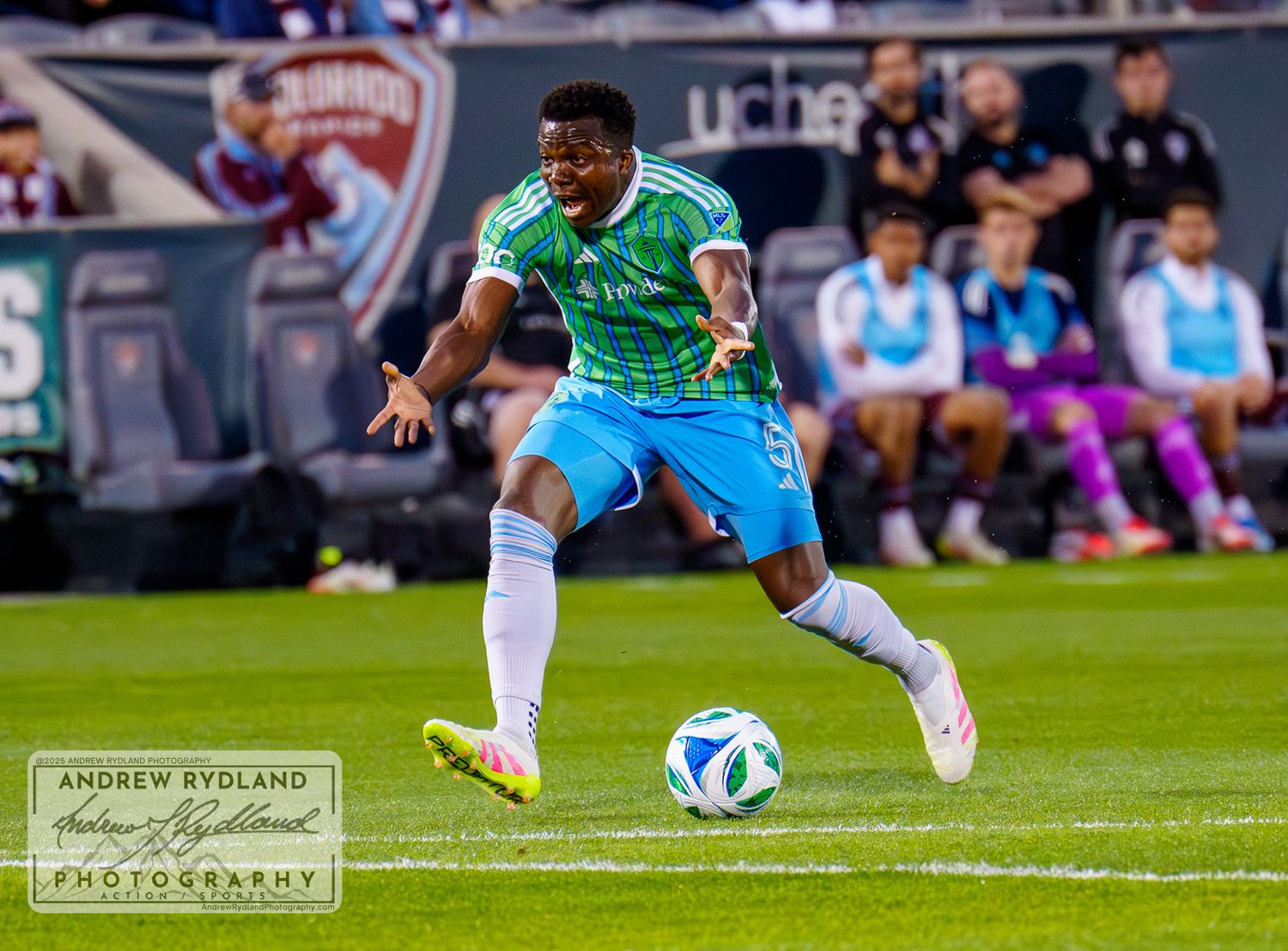 Soccer player in bright green jersey and blue shorts dribbling ball on soccer field during match.