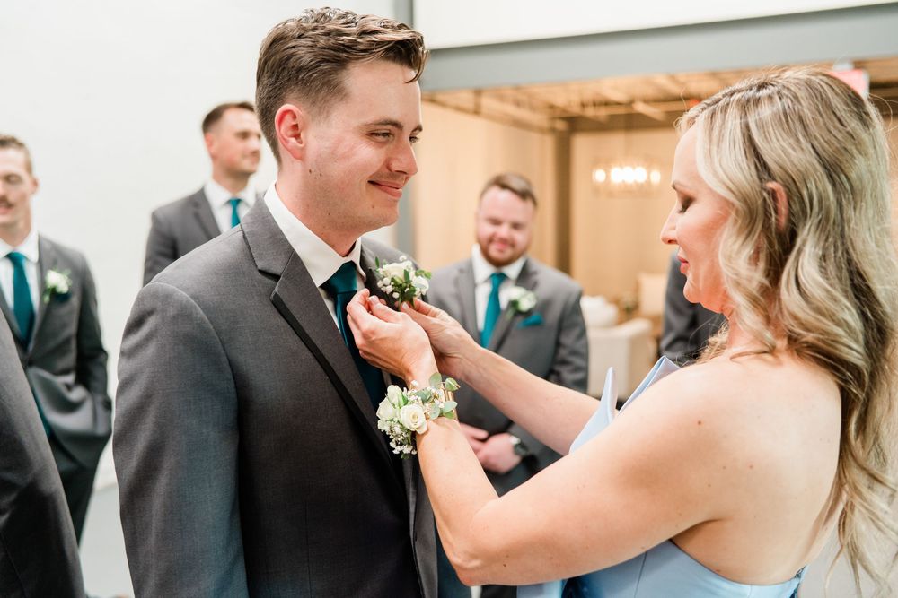 White and blush floral boutonniere is pinned to a grey suit jacket during an elegant wedding ceremony.