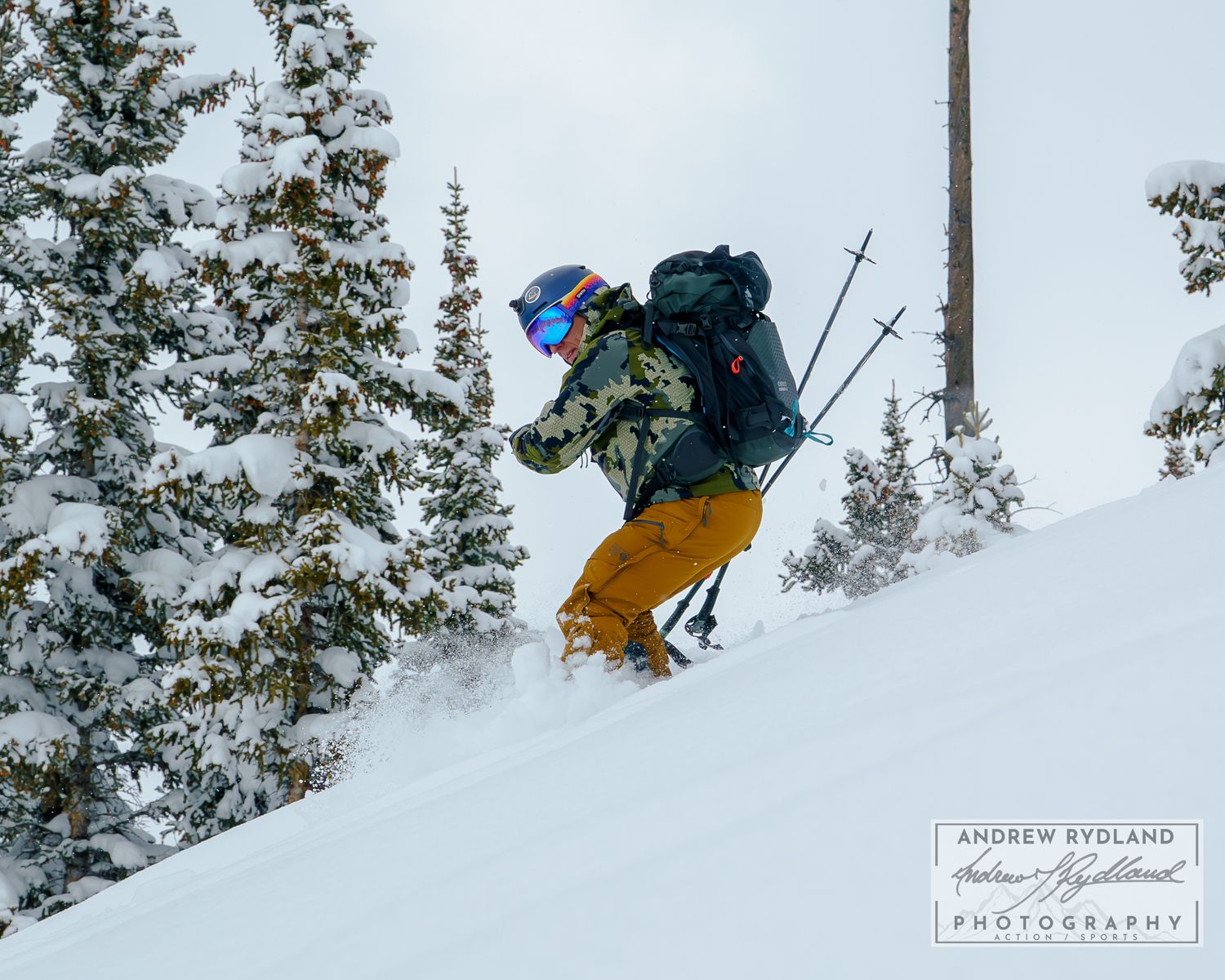 Skier in yellow pants and colorful helmet performs jump maneuver in snowy winter landscape.