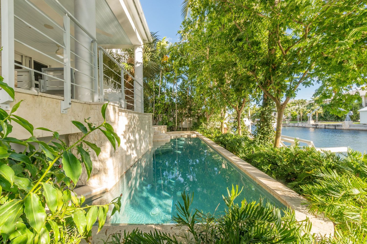 Lush tropical landscaping surrounds modern waterfront property with pool.