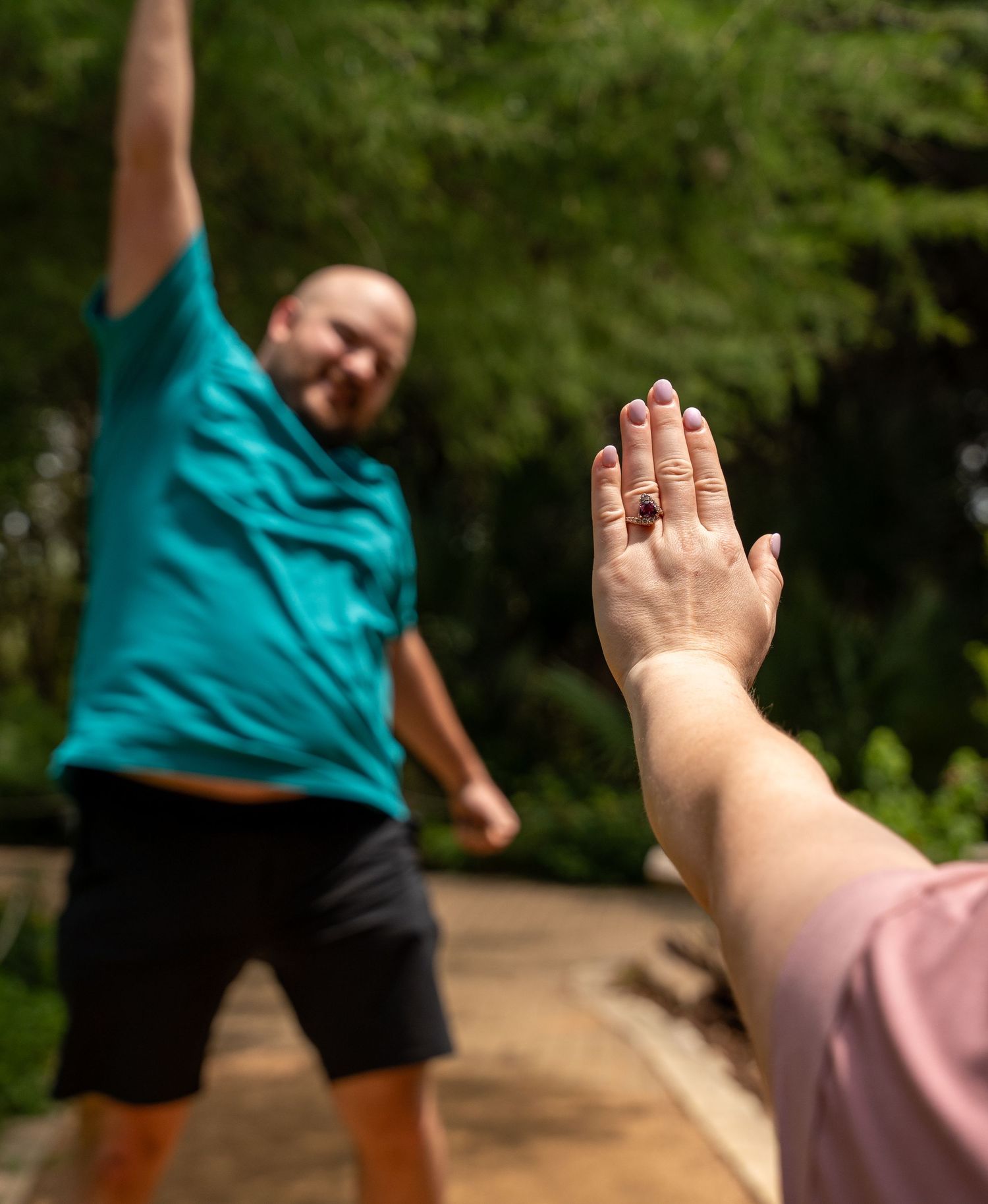 Two people high-fiving in an outdoor park setting with green trees and foliage in the background.