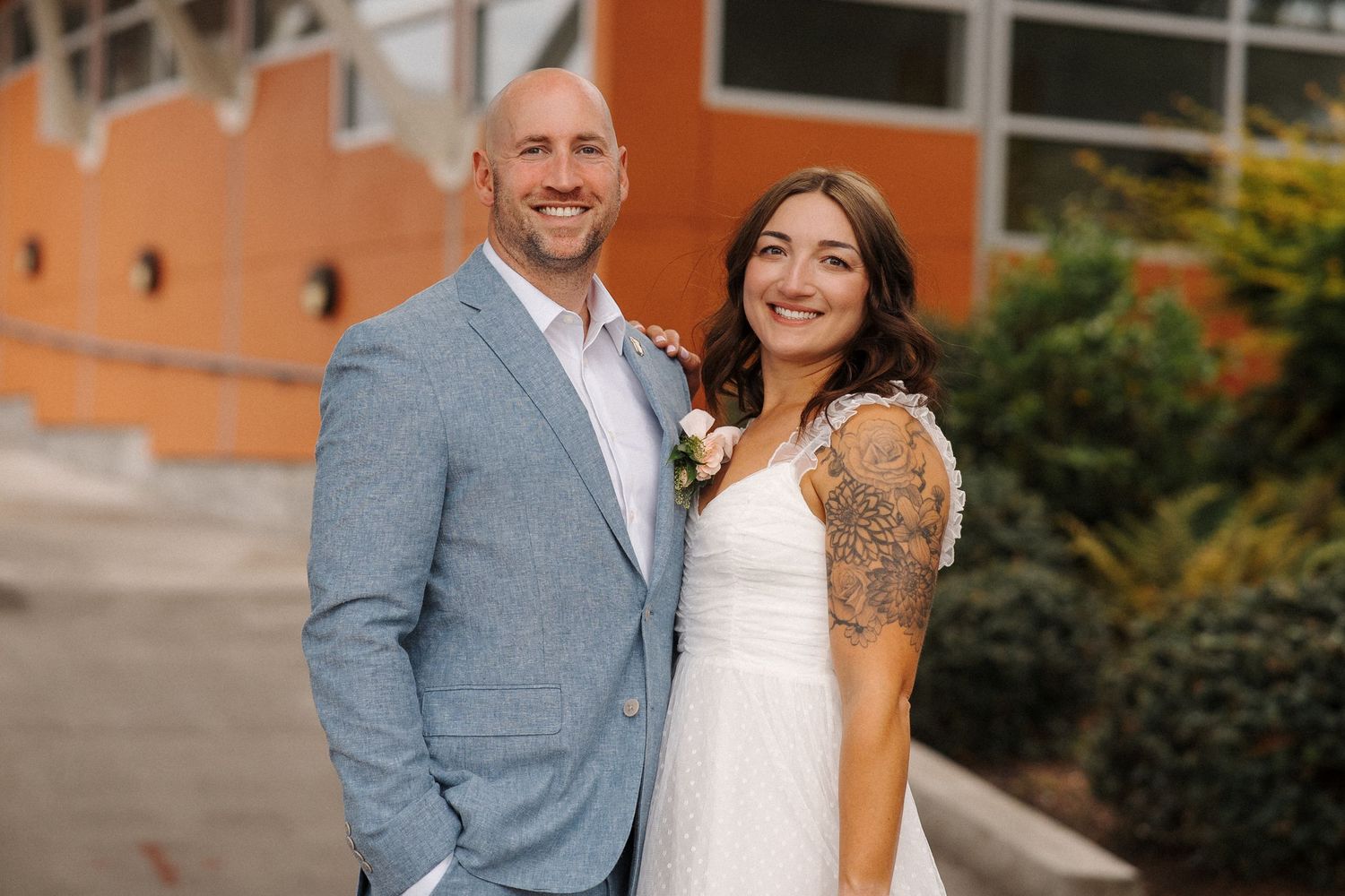 Couple in wedding attire share a happy moment outside a brick building on their special day.