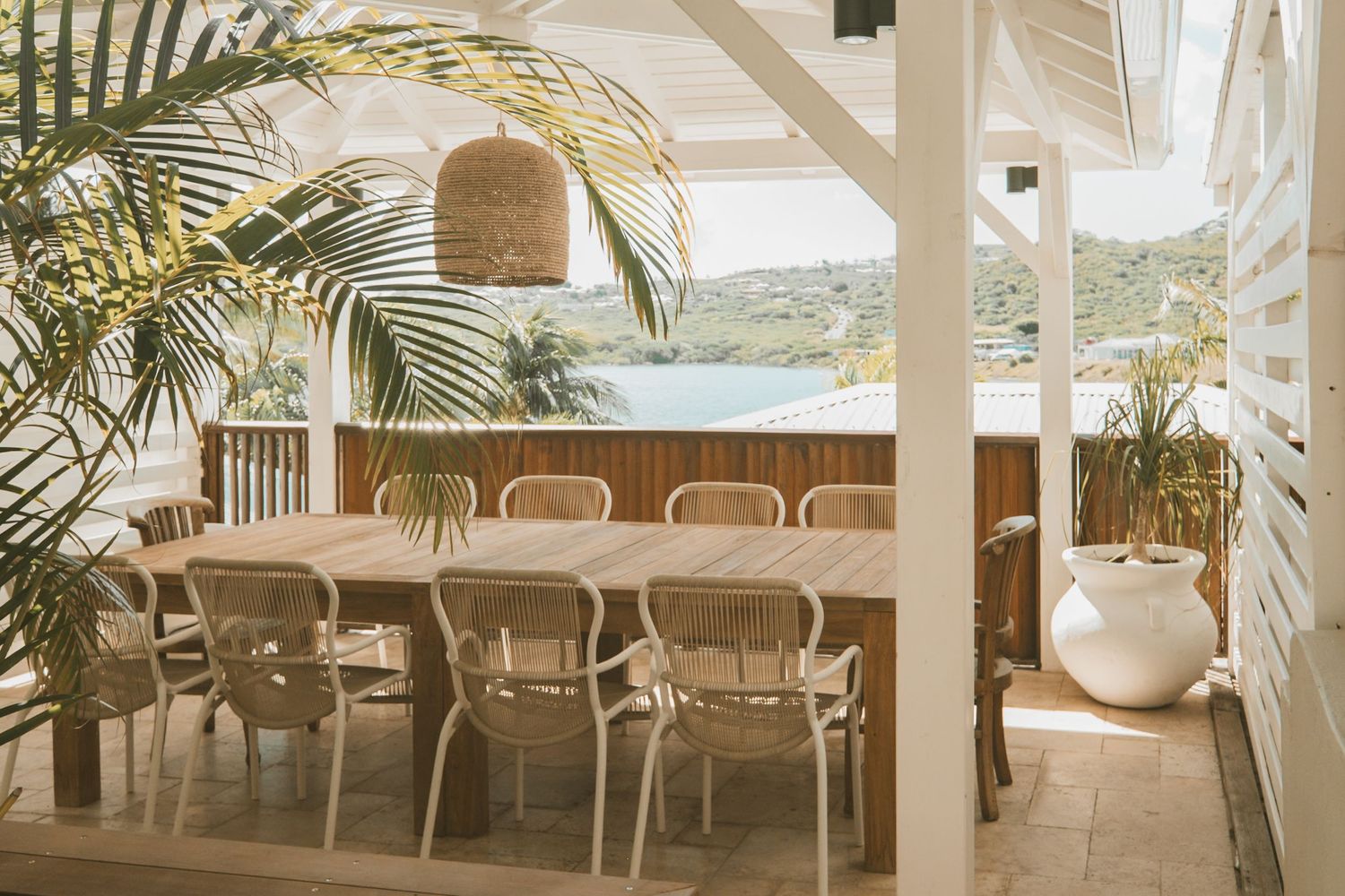 A long white covered patio area with palm trees and casual seating arrangements overlooks an outdoor view.