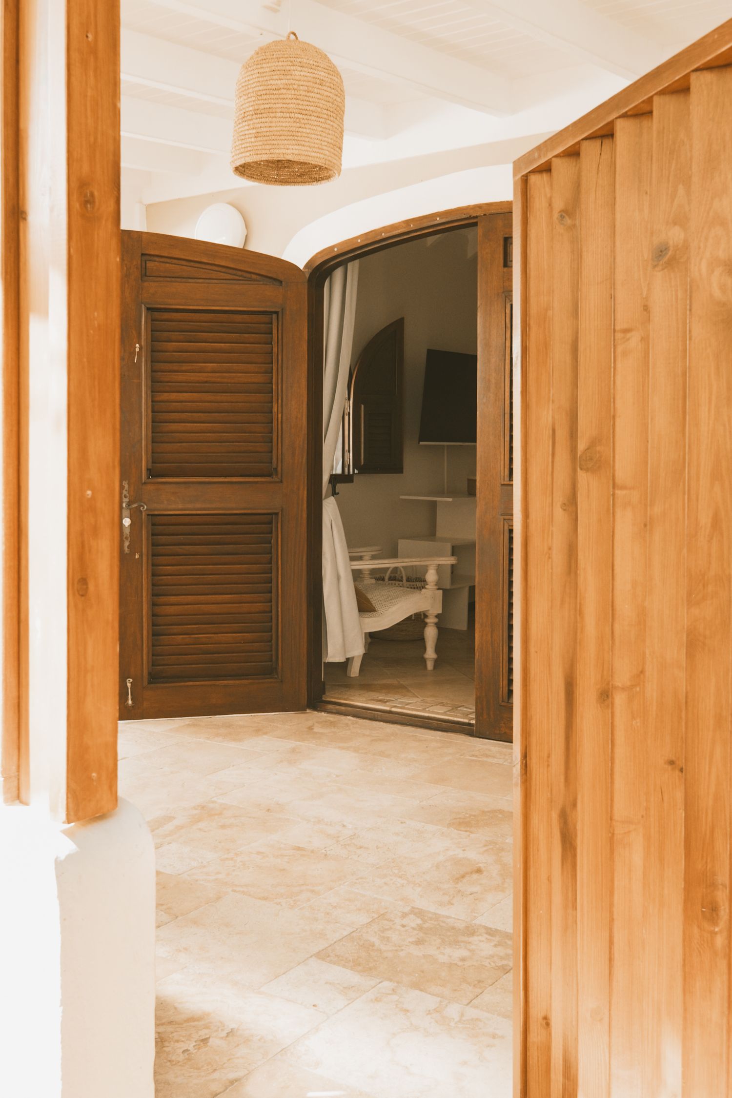 Open wooden doors reveal a bright interior space with modern decor and a woven pendant lamp hanging above.