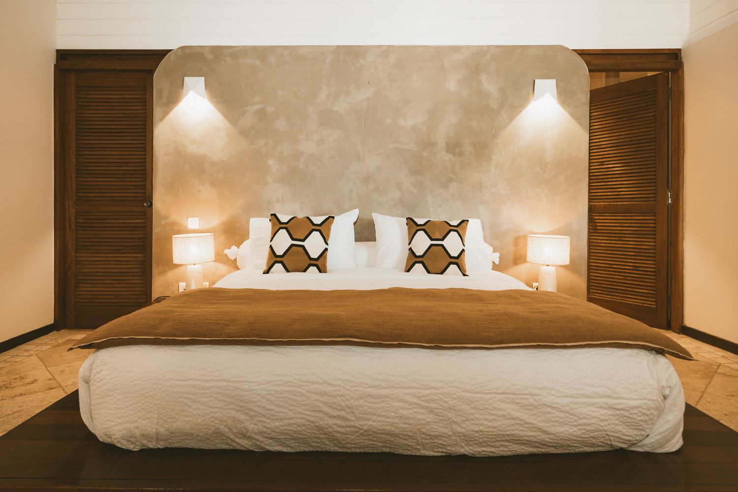 Modern hotel bedroom with neutral beige tones featuring luxurious white bedding and ambient lighting.
