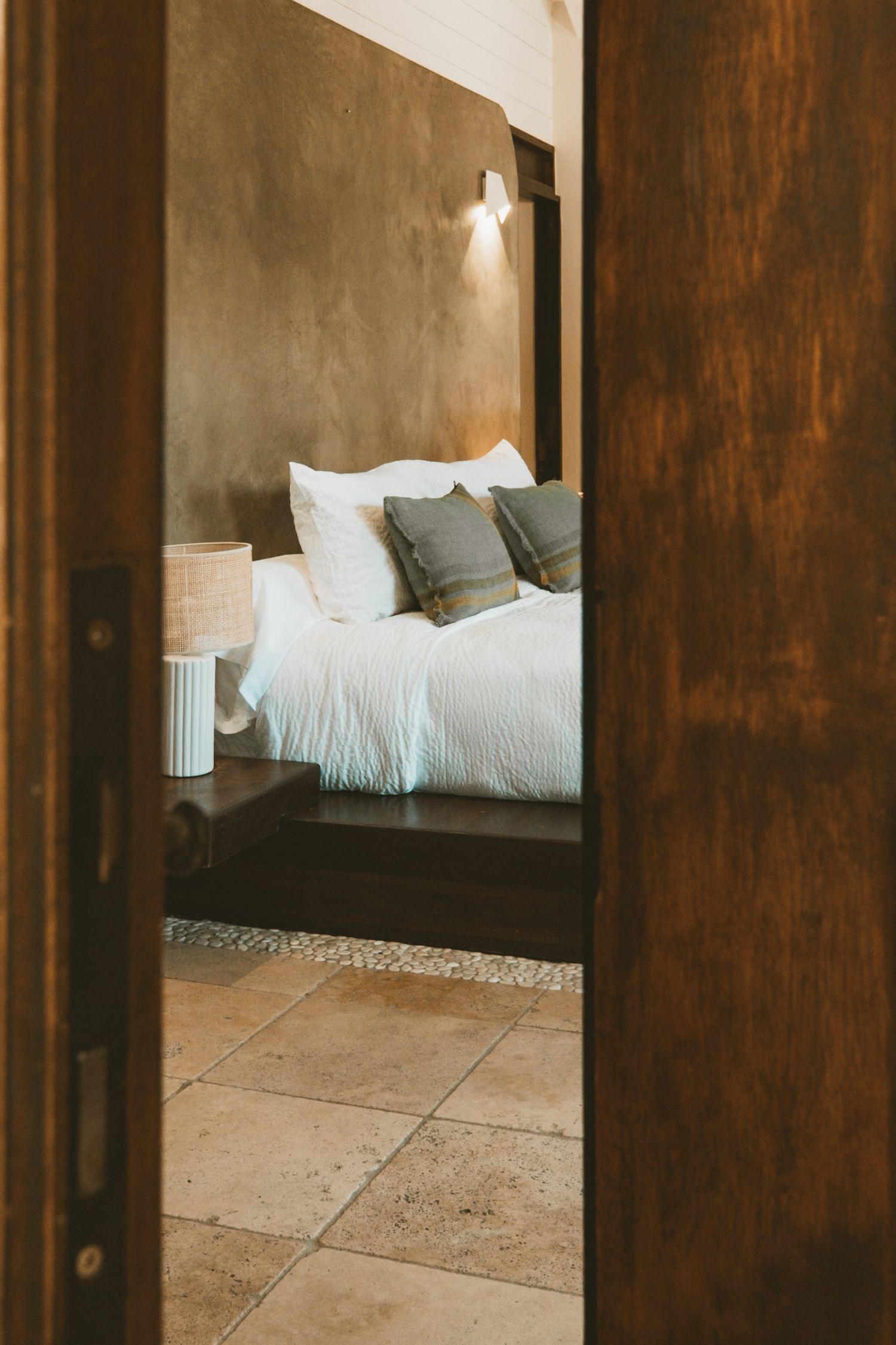 Modern bedroom interior with dark wood sliding doors and white bedding visible through doorway panels.