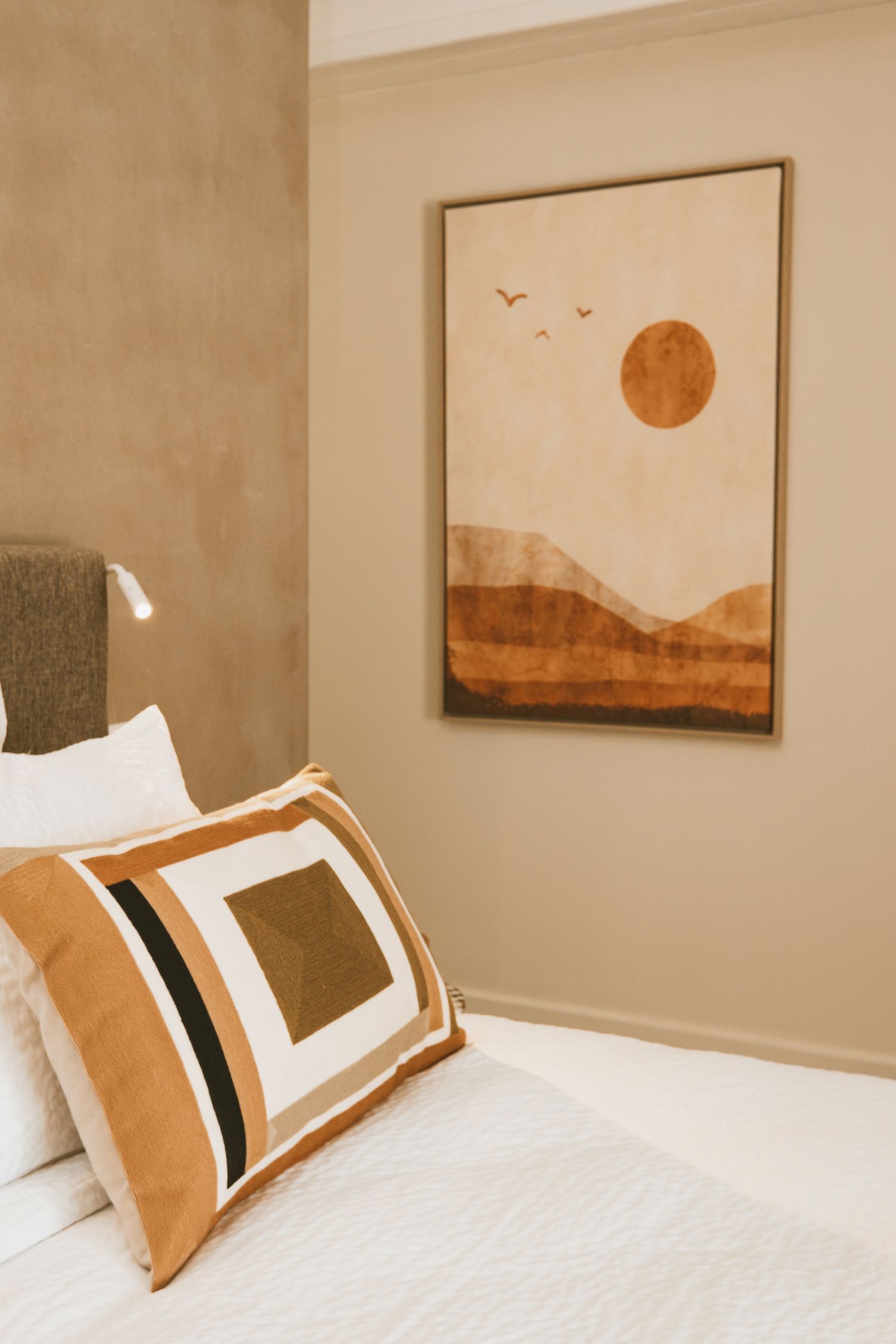 A set of four photos showing modern hotel room art with minimalist earth-tone landscapes mounted above a white bed.