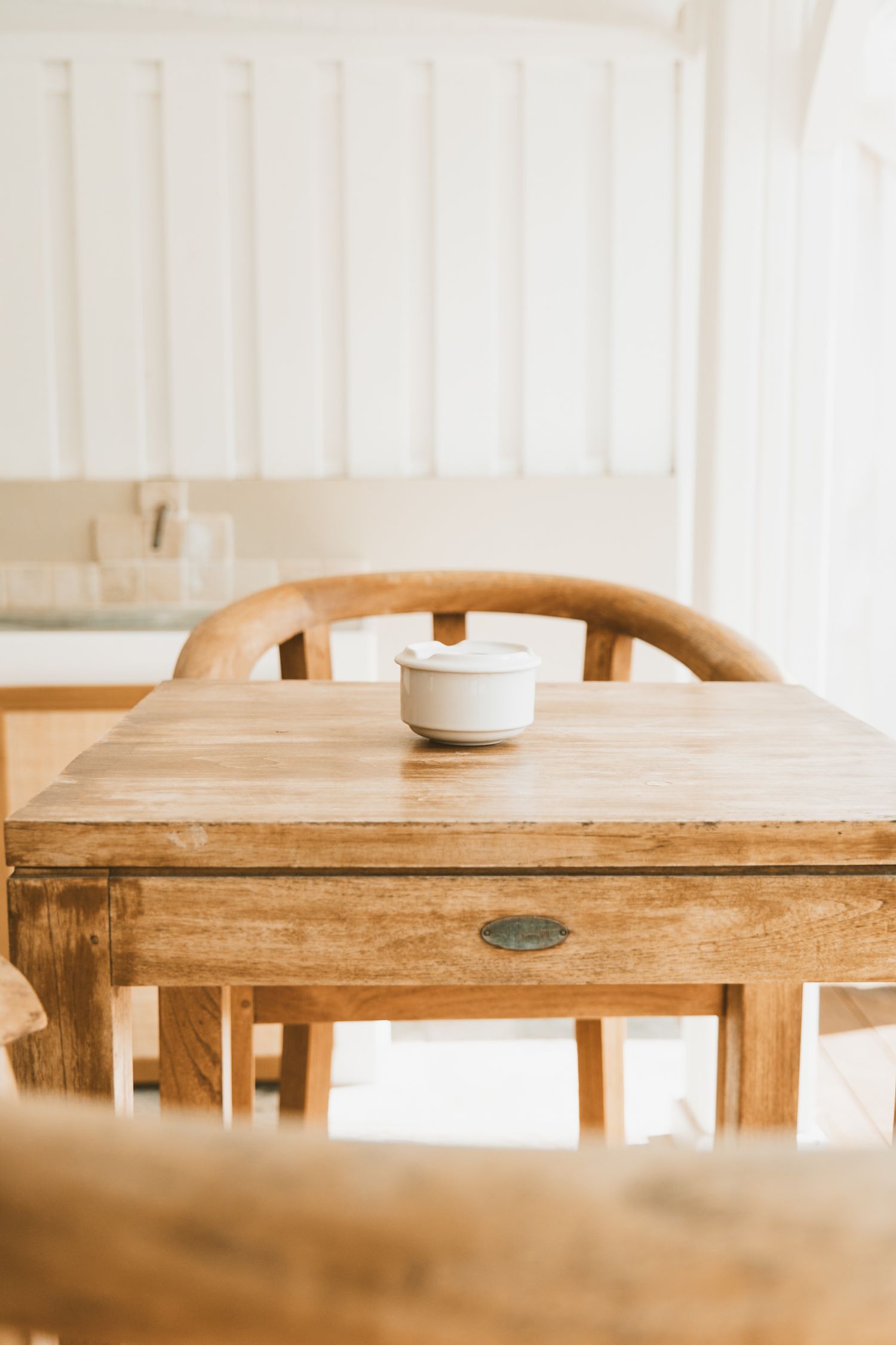 Rustic wooden dining table with chairs and small white bowl in minimalist beige interior setting.