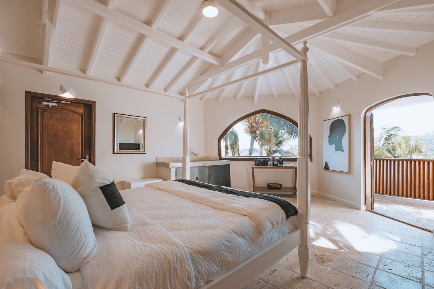 Bright and airy luxury bedroom with vaulted white ceiling, arched windows and a private balcony overlooking tropical views.