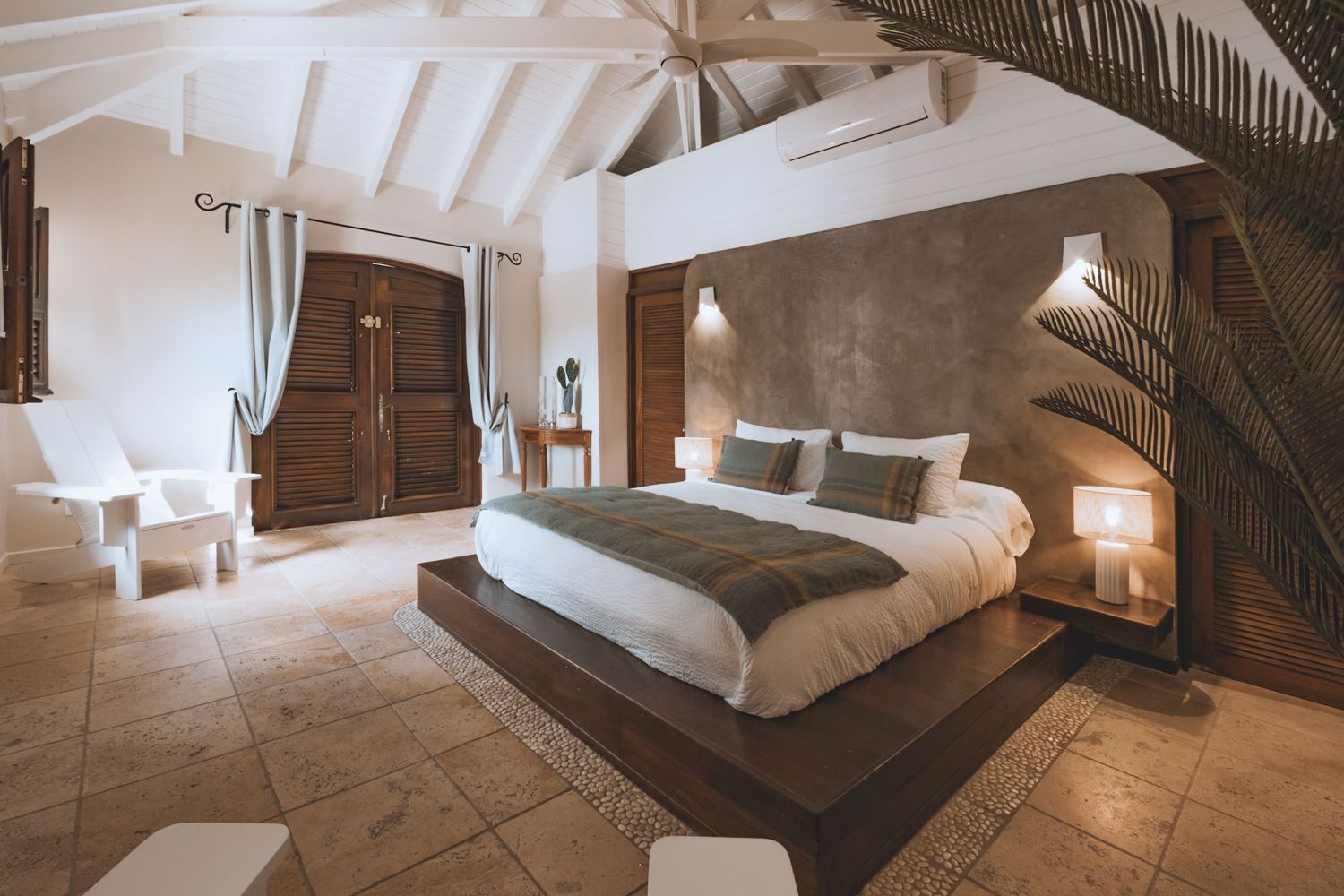 Luxurious modern bedroom with white beamed ceiling, stone floors, and potted palm plant in a minimalist design.