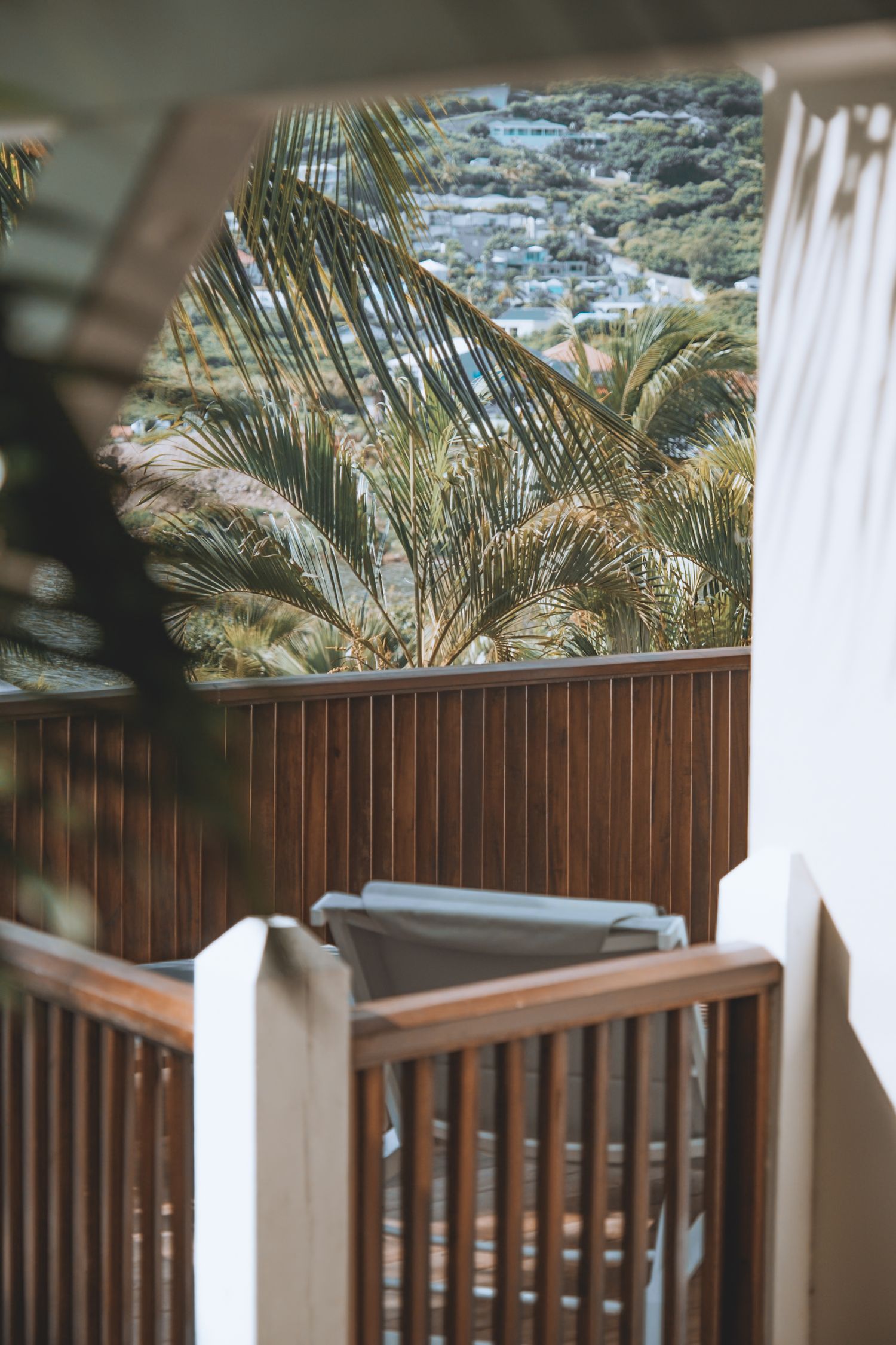 White wooden porch railing against tropical palm fronds and ocean view creates serene coastal ambiance.