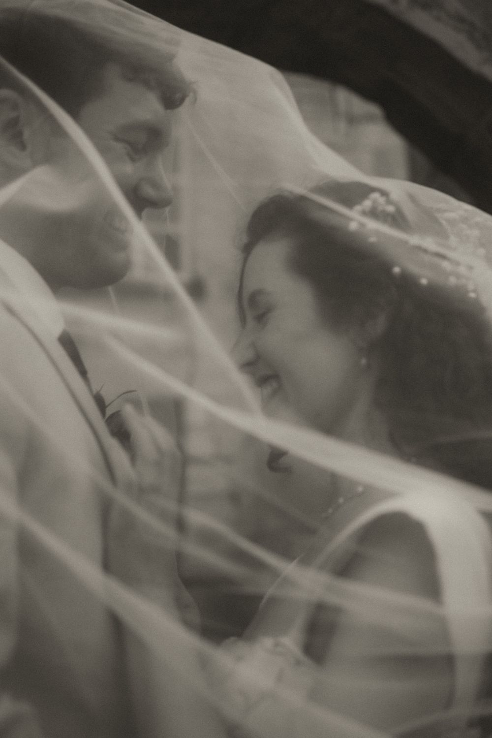 Black and white photo of a bride and groom sharing an intimate moment under a flowing wedding veil.