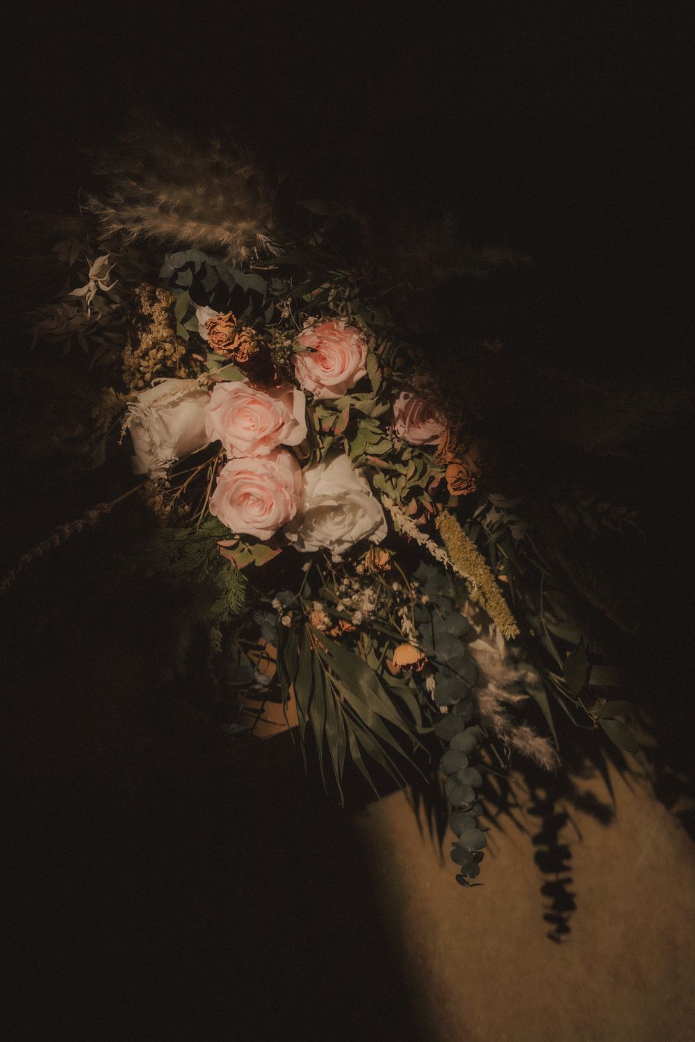 Moody floral bouquet with pink roses and greenery in dramatic dark lighting.