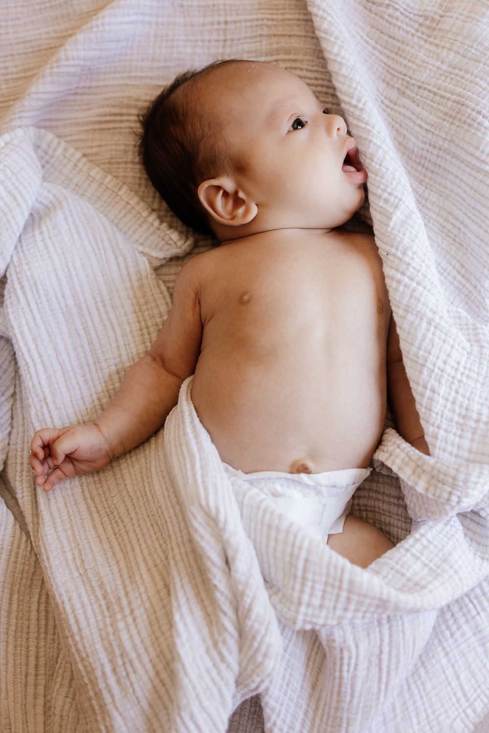 A sleeping baby wrapped in soft white muslin blankets - San Jose newborn photography