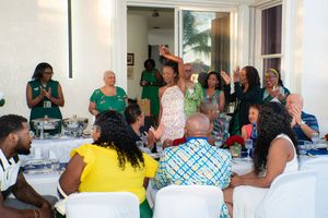 Guests celebrating at an indoor gathering with a woman raising her hand in a festive green-themed event.