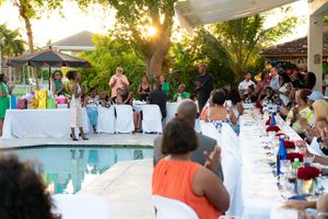 Outdoor poolside dinner party at sunset with long decorated tables and guests gathered together.