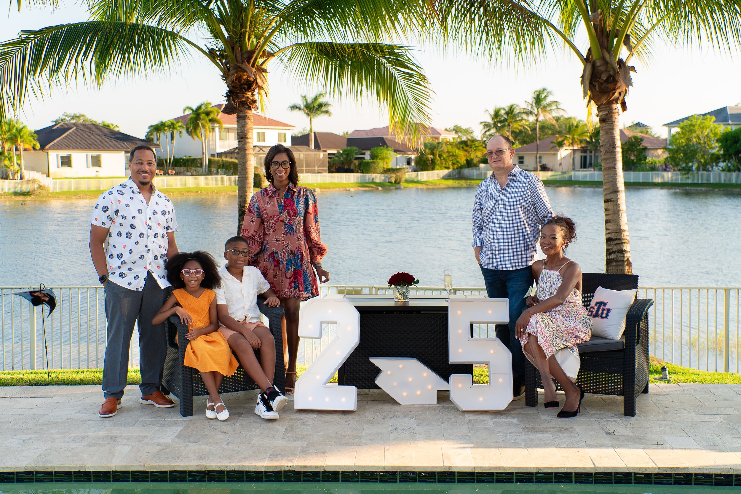 Family group photo outdoors by a pool with decorative number 25 marquee letters and palm trees.