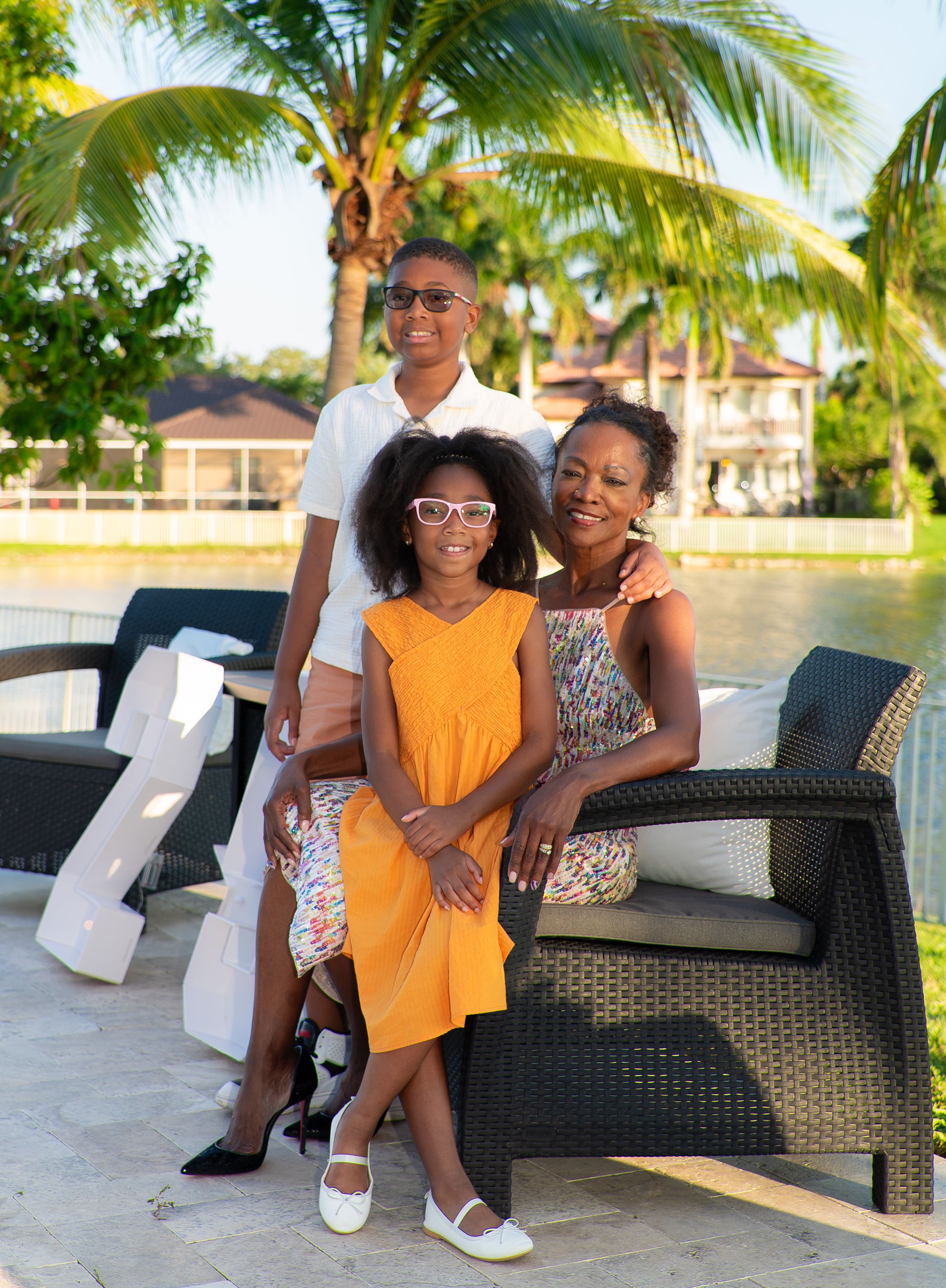 Family of three posing outdoors by a tropical waterfront with palm trees in Miami, Florida.