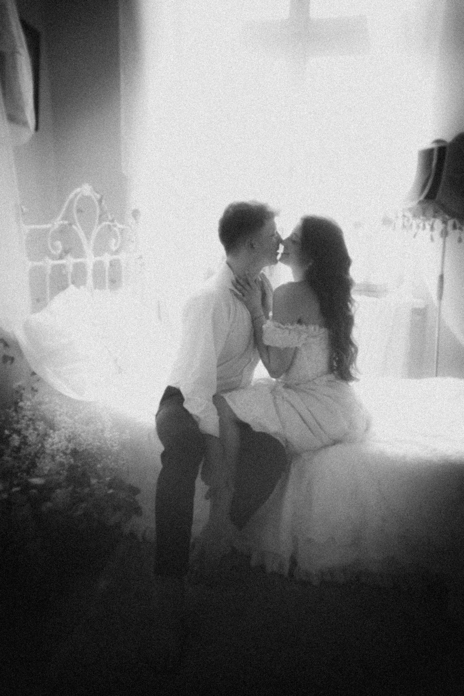 A romantic black and white photograph of a couple in wedding attire sharing an intimate moment in soft lighting.