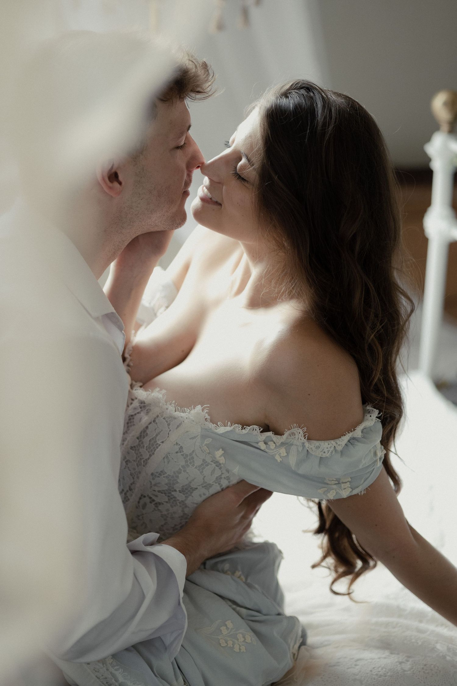 A romantic couple in formal wedding attire share a tender kiss in soft natural light.