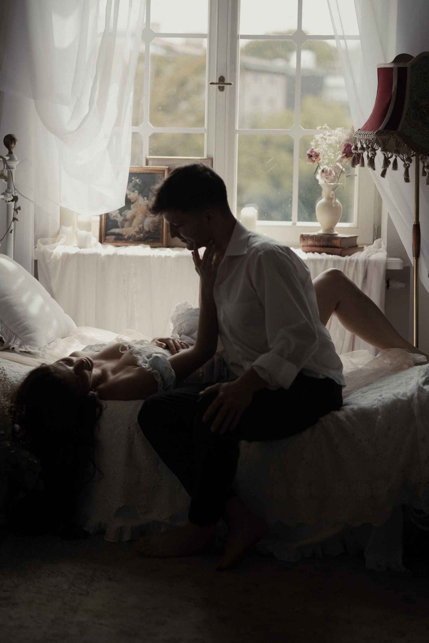Moody vintage-style bedroom scene with window light, curtains and floral vase creating romantic ambiance.