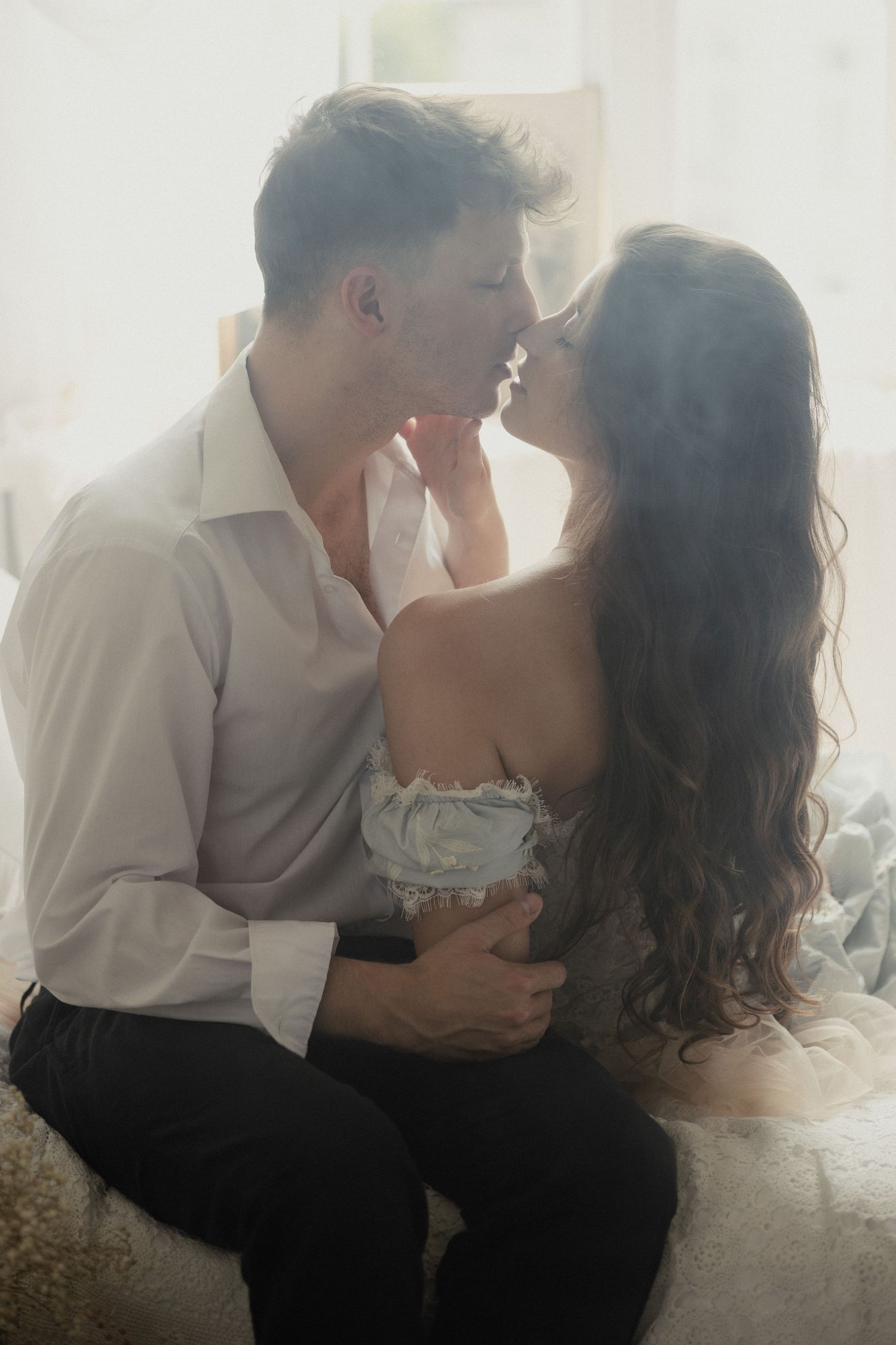 A romantic couple shares intimate moments while sitting together in a dreamy, soft-lit setting.
