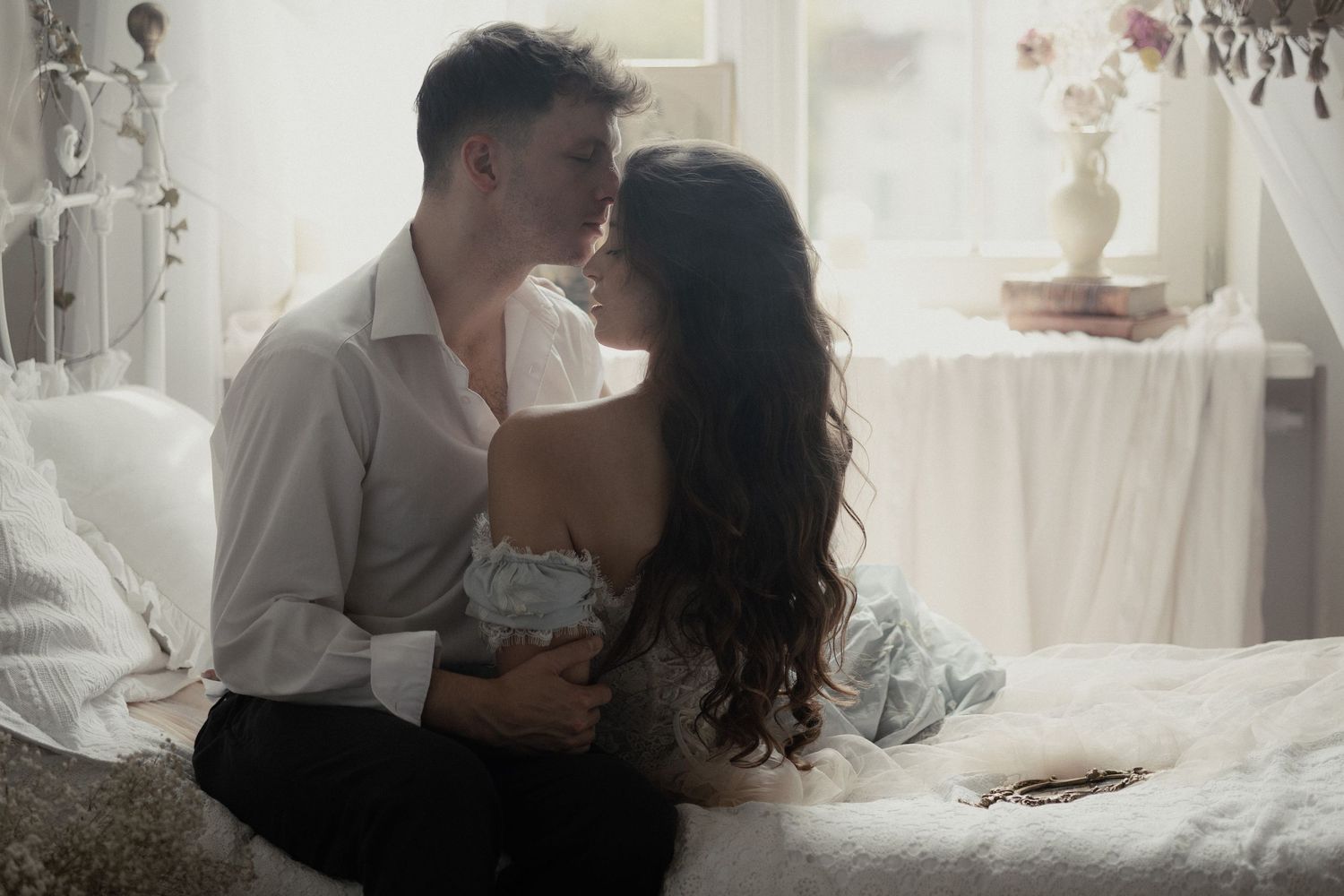 Couple sharing intimate moments on bed in soft lighting through multiple romantic photograph frames.