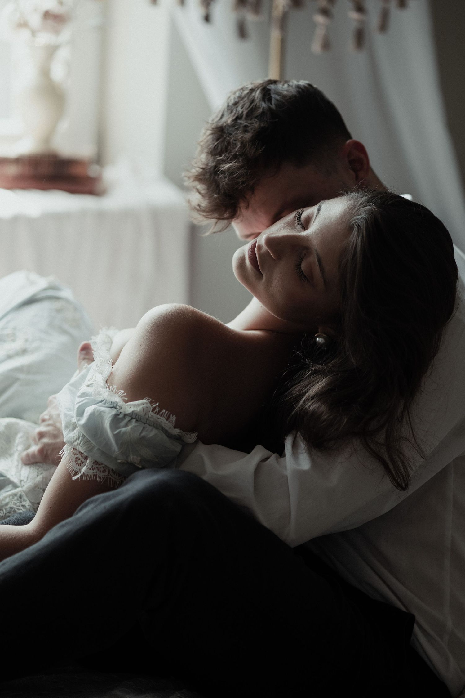 Moody black and white photo series showing a romantic couple embracing in bed against soft window light.
