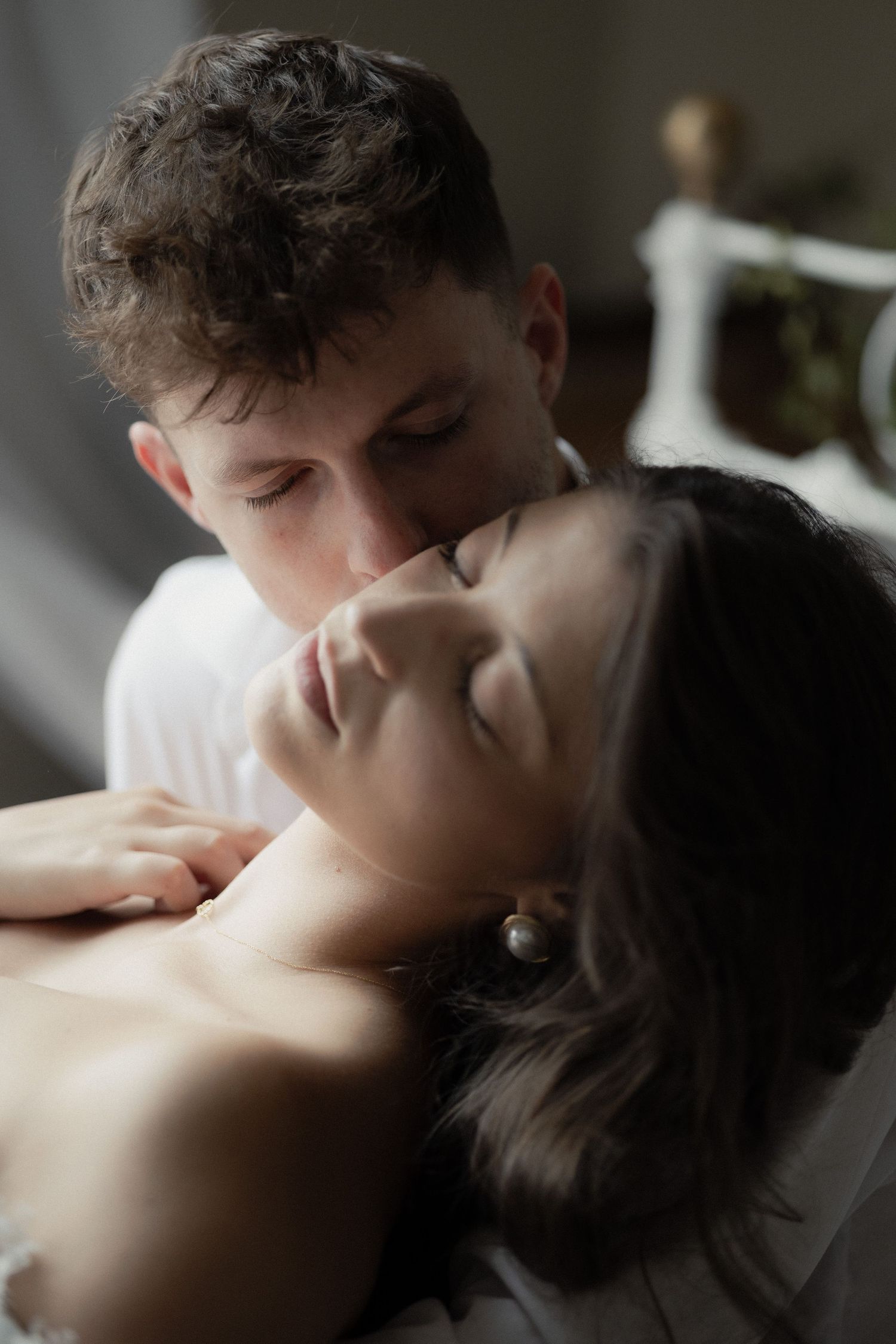 A tender intimate portrait of a couple embracing in a dreamy, atmospheric indoor setting.