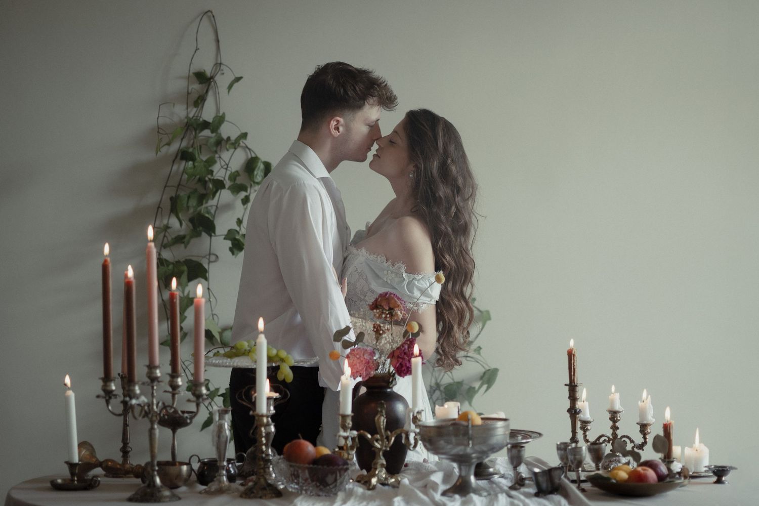 Romantic wedding couple embracing by candlelit table with vintage candelabras and floral arrangements.