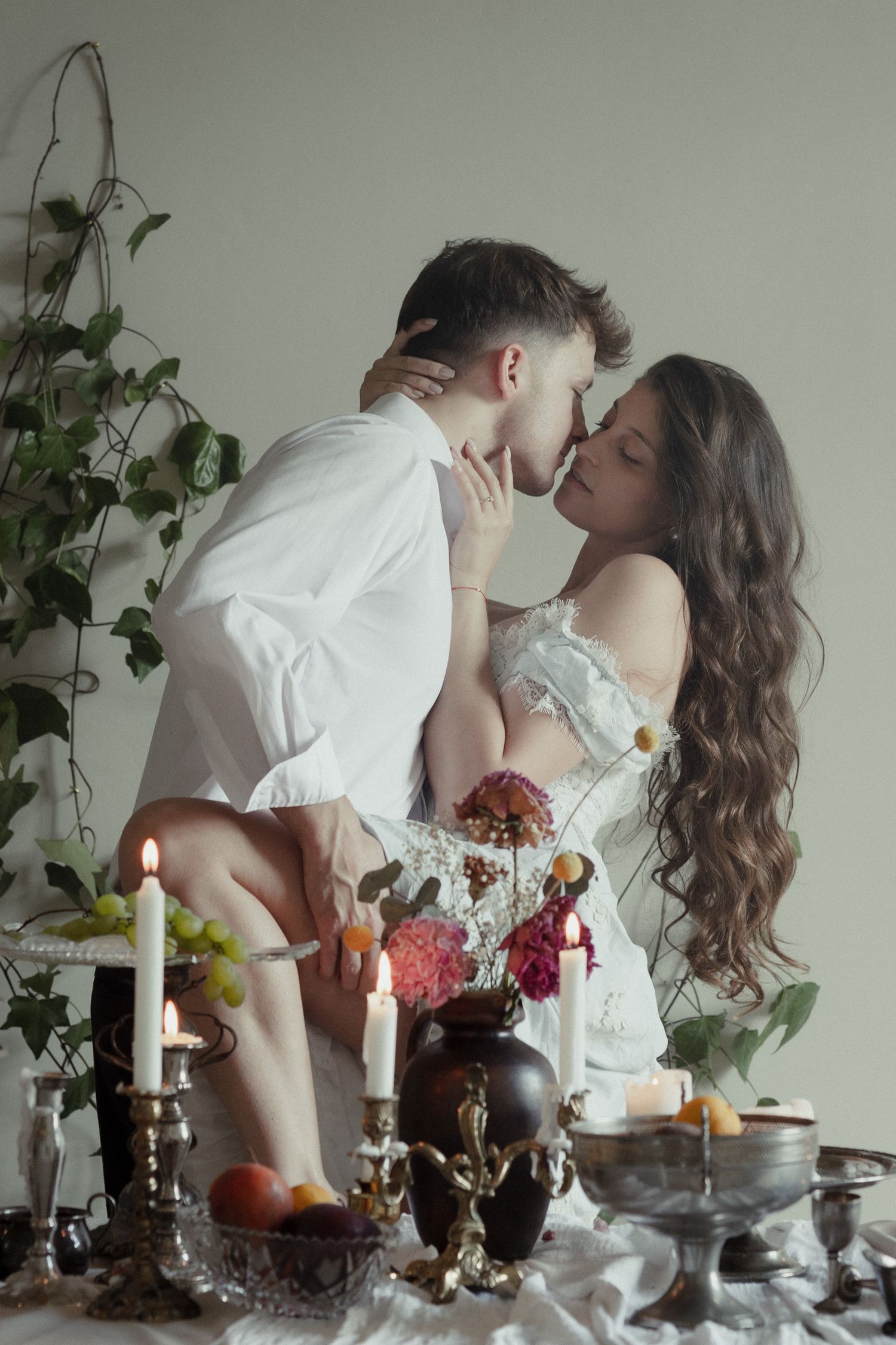 A romantic couple shares an intimate moment at a candlelit table decorated with flowers and desserts.