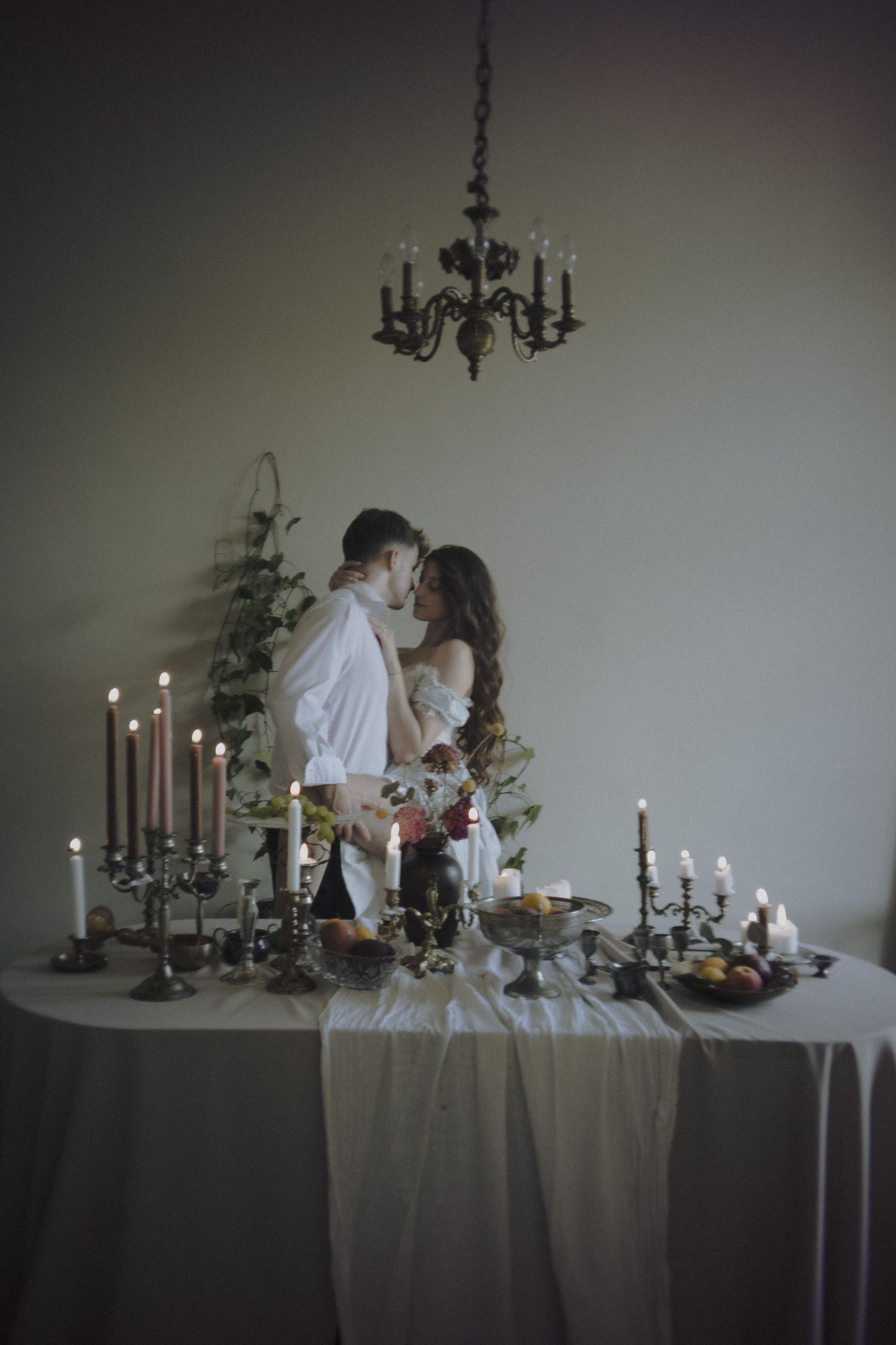 A romantic candlelit table setting with elegant black candelabras and white draping creates a moody atmosphere.