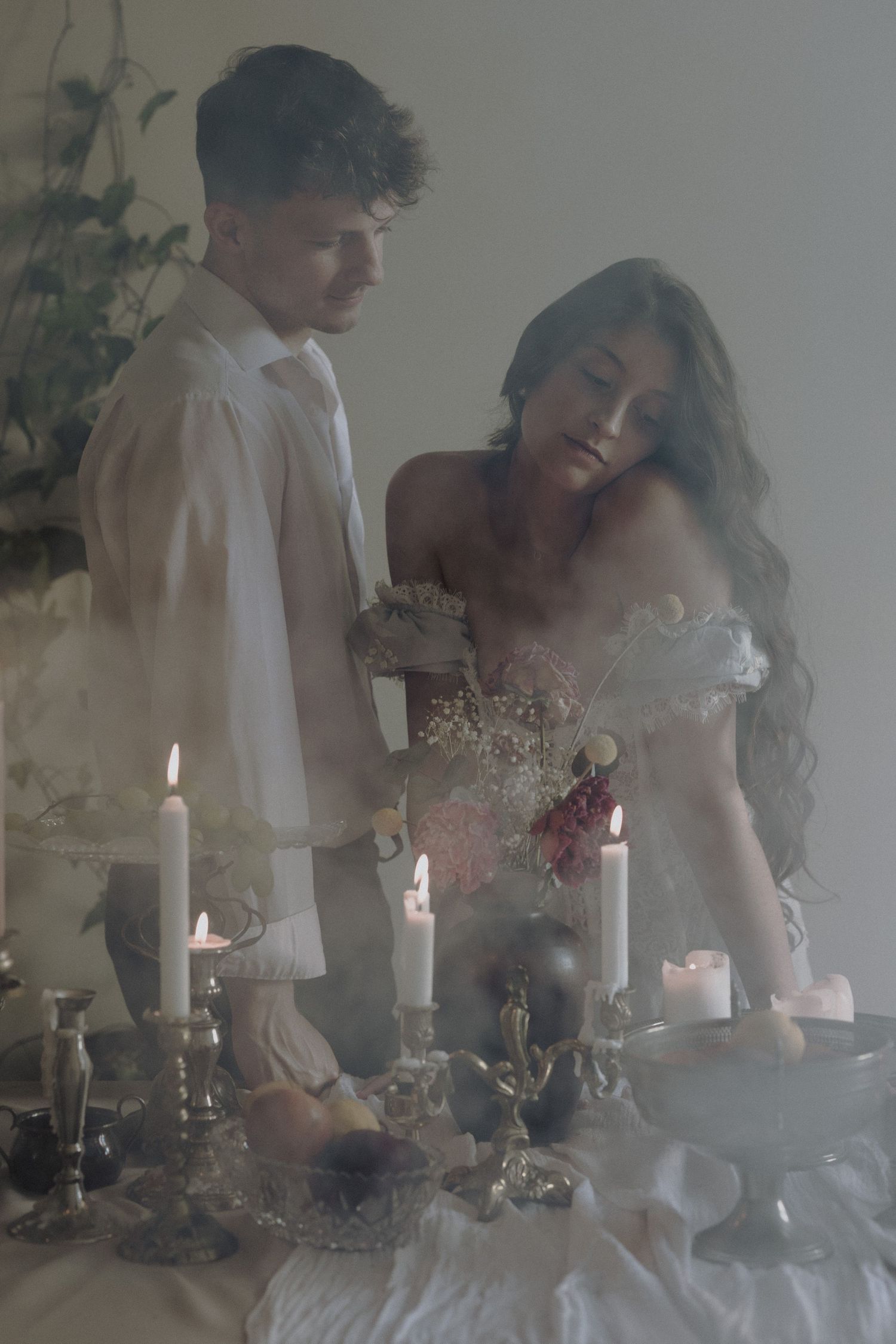 Ethereal wedding scene with candles and babys breath flowers on table as couple leans over romantic vintage-style setting.