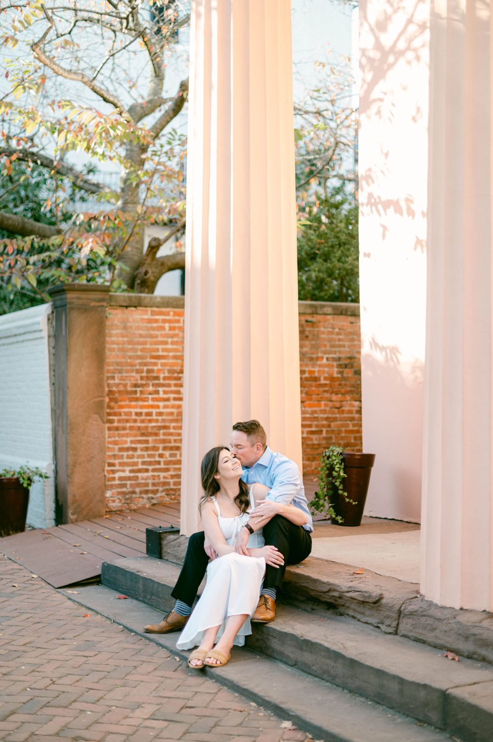 Couple sitting on brick steps against white columns in warm sunlight.