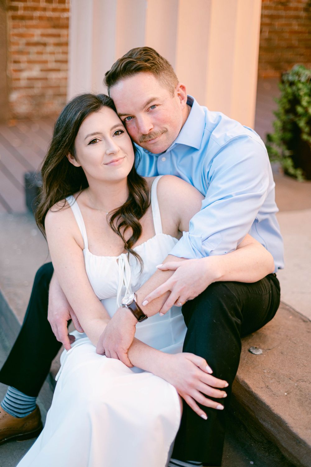 A romantic couple embraces while sitting on brick steps during an engagement photoshoot.
