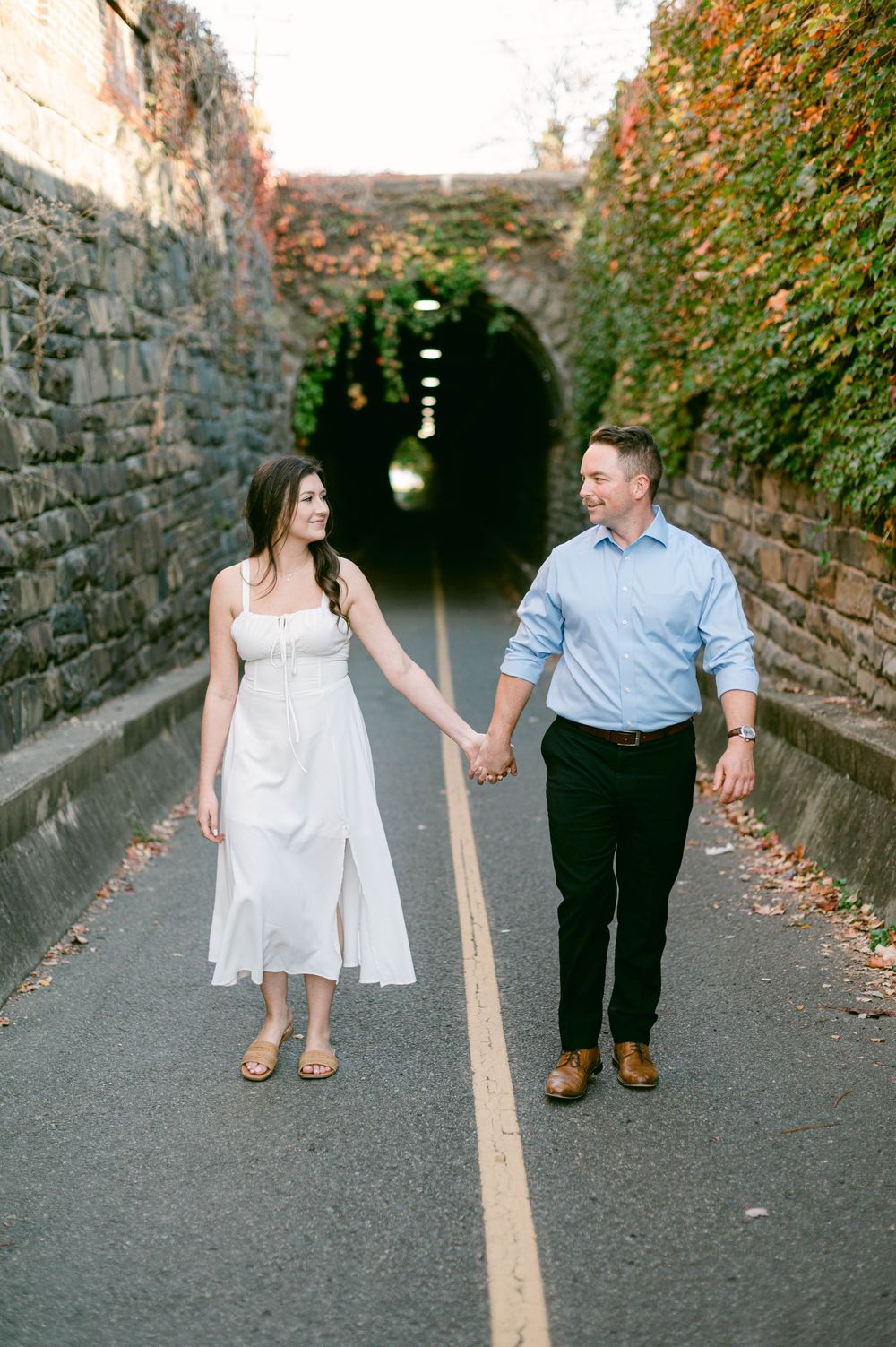 Couple walking hand in hand through a tunnel lined with ivy during photo session.